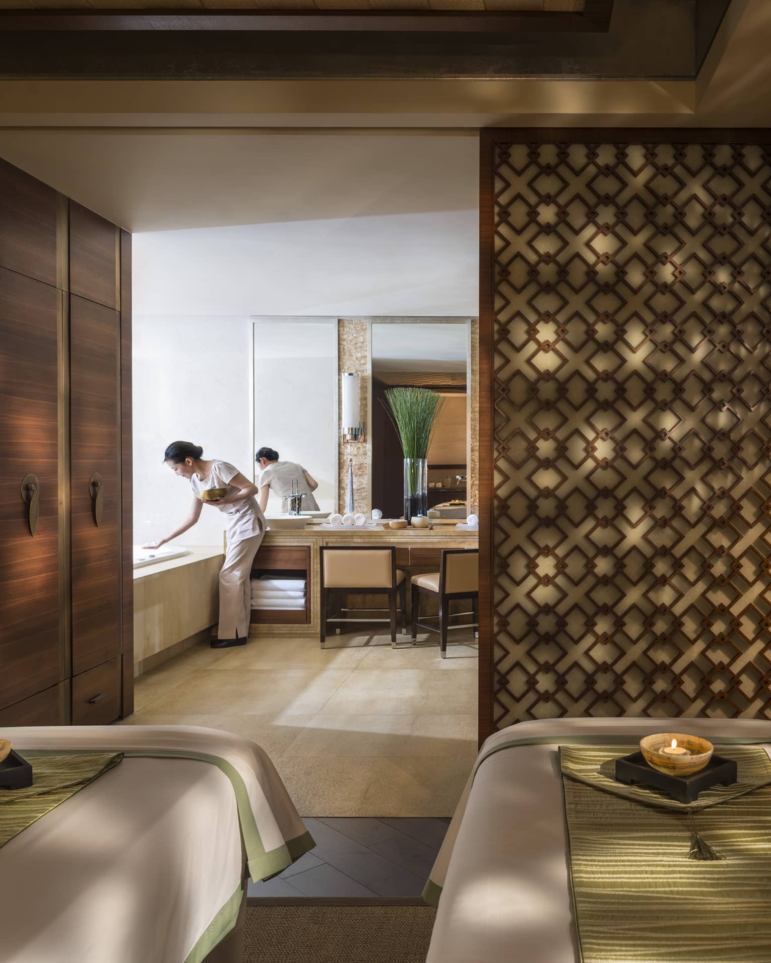 Couples massage beds side-by-side in spa room with candles and staff preparing bath