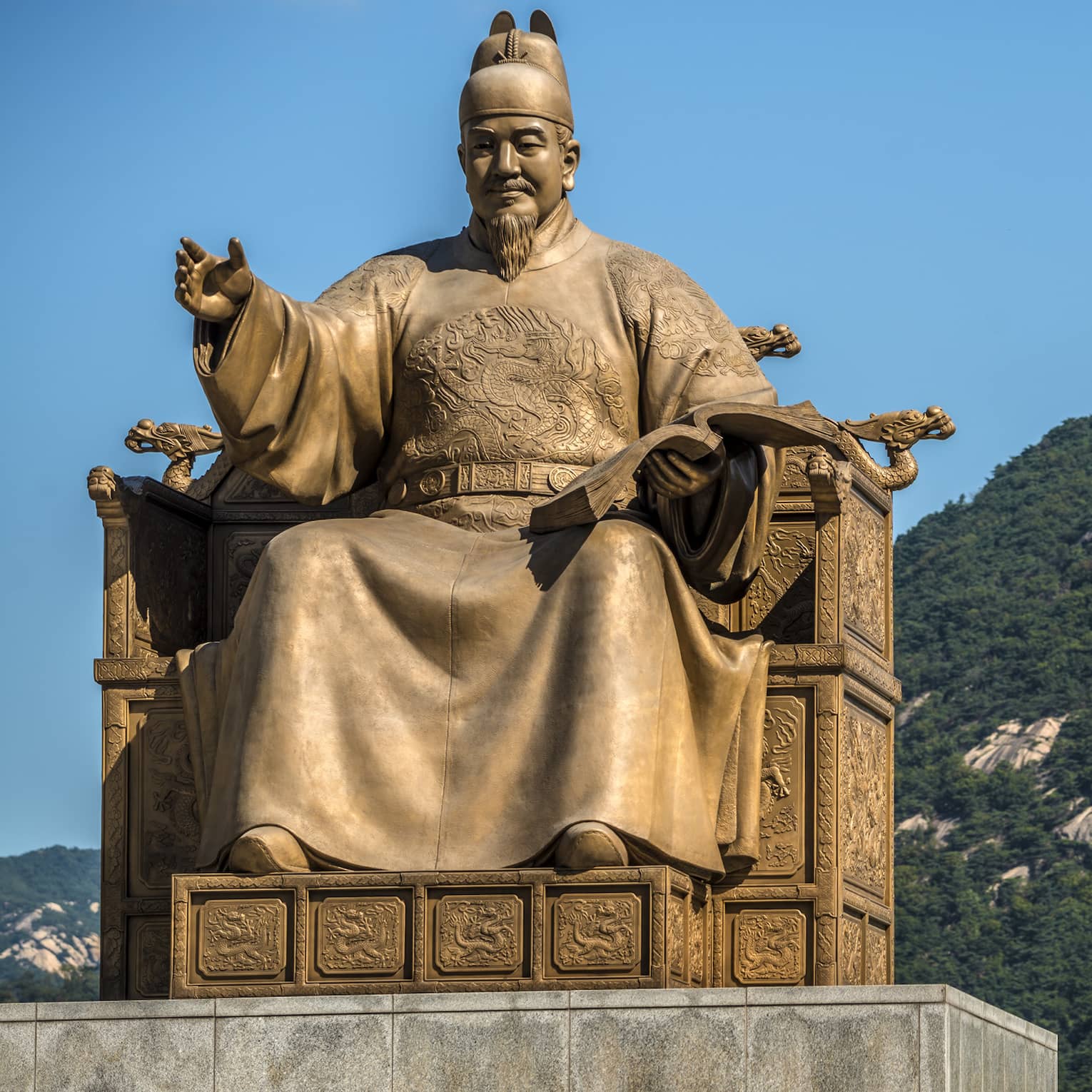 Golden statue of Sejong the Great, cloudless blue sky, lush green mountains in the background