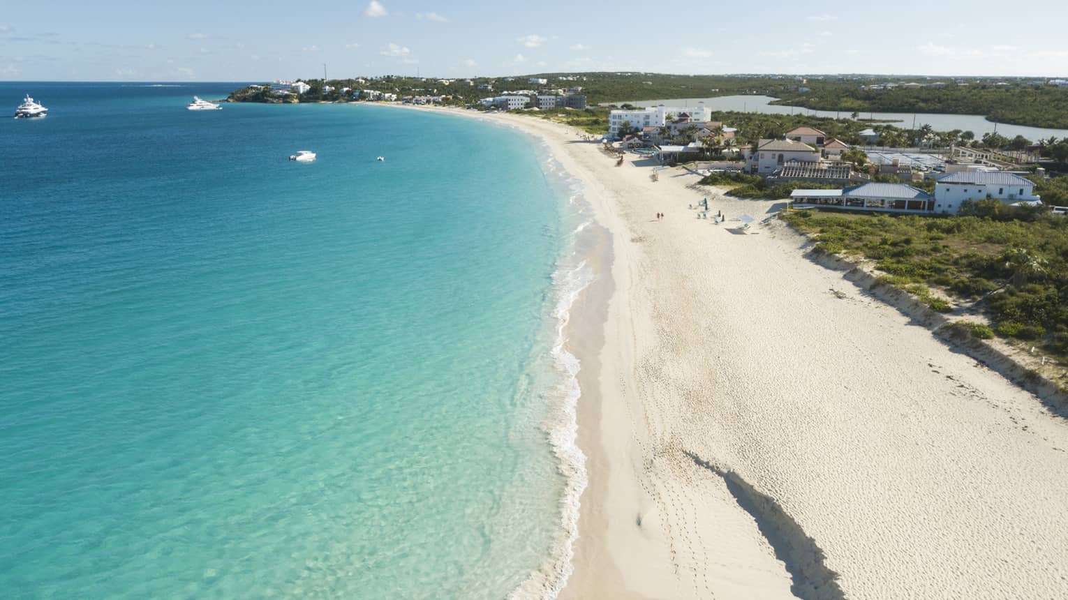 long stretch of white sand beach with crystal blue waters with a hotel resort on the shore