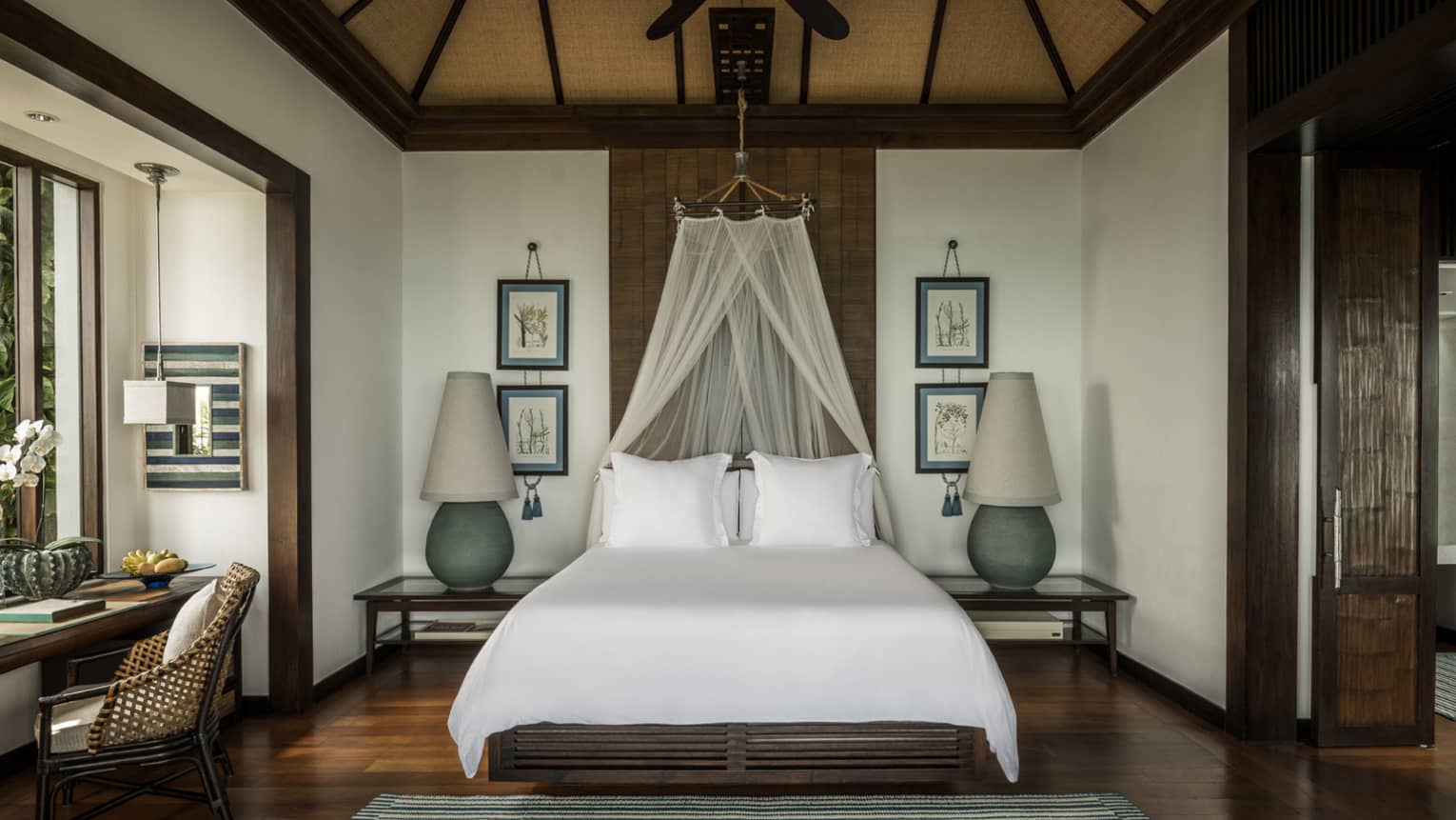 Family Pool Villa bed with white net canopy, large lamps on each side, wood floors, desk by window