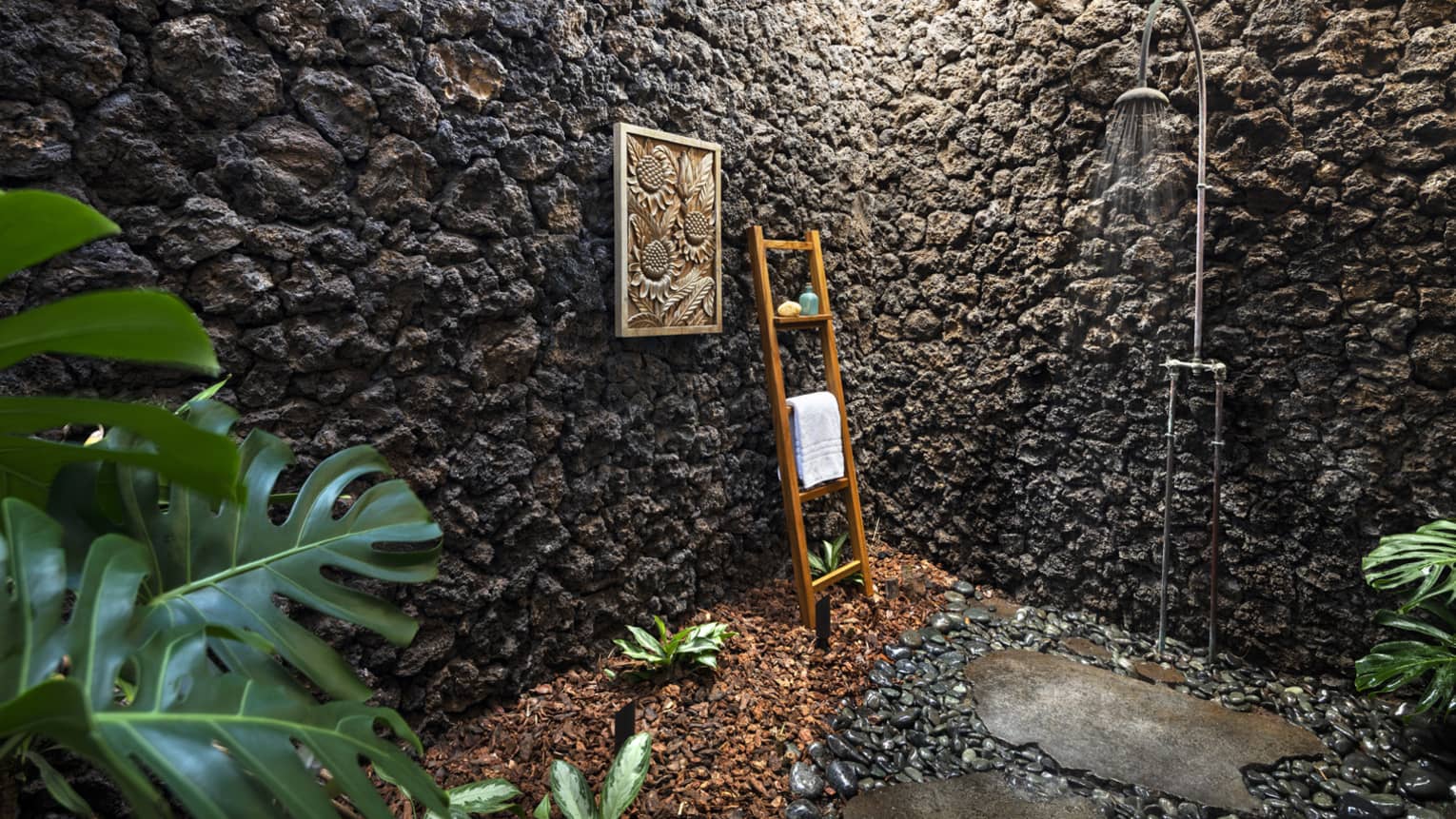Outdoor shower with stone walls, teak ladder holding towel, greenery