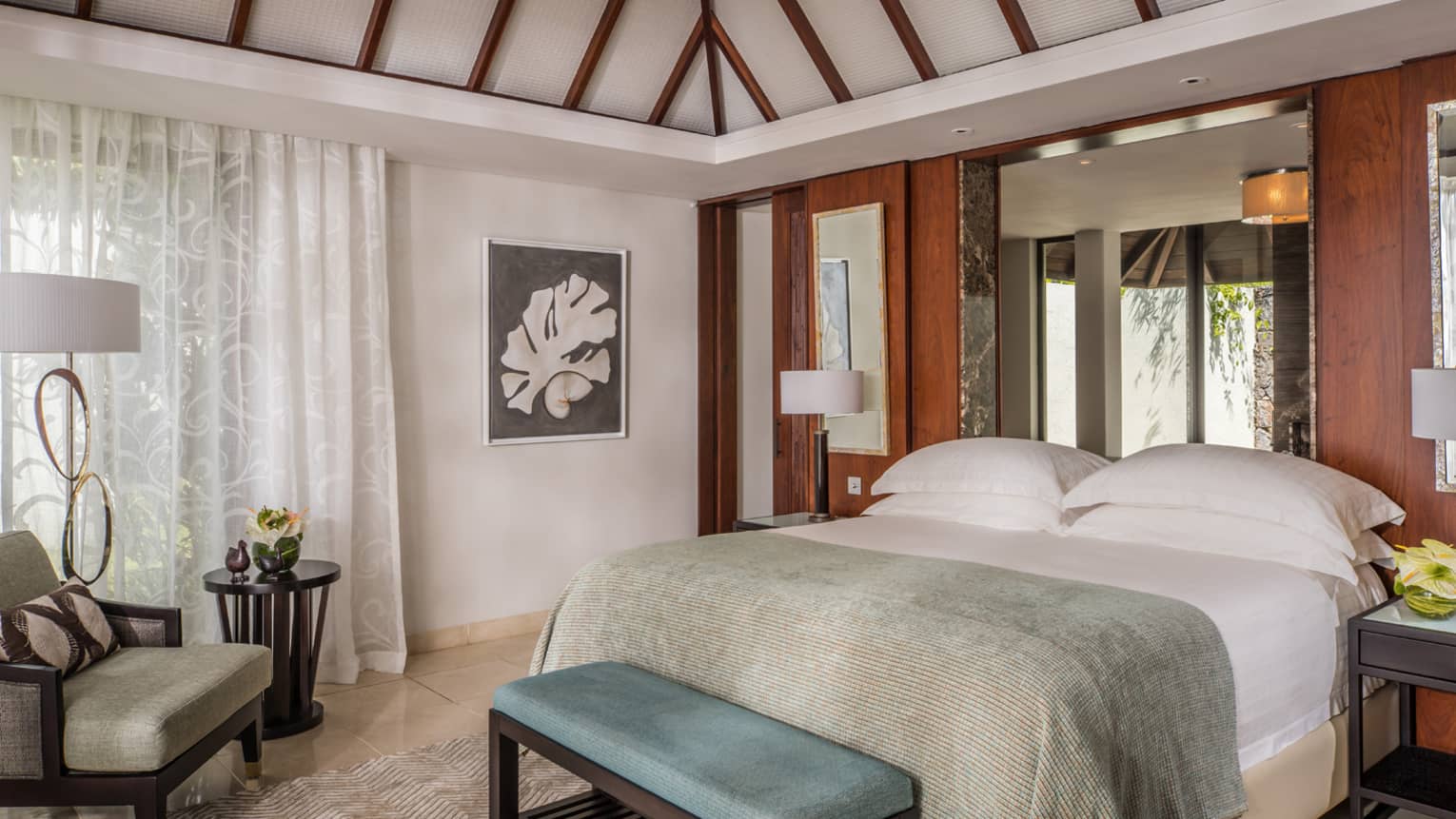 Residence Villa bed with light blue blanket, bench, armchair by drawn sheer white curtains
