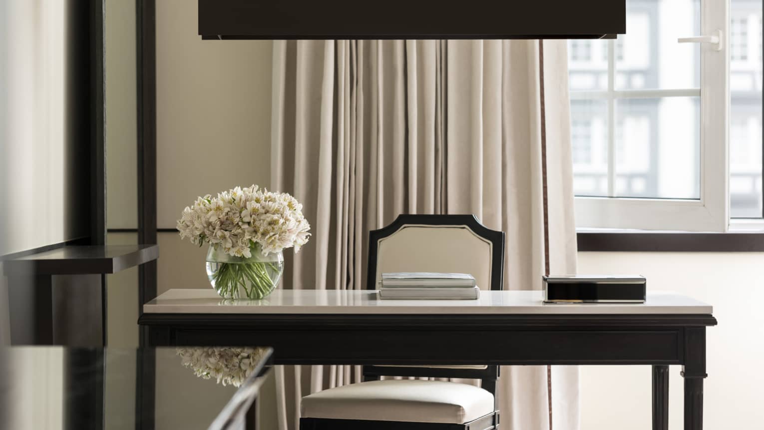 Writing desk with a floral arrangement and upholstered chair by the window