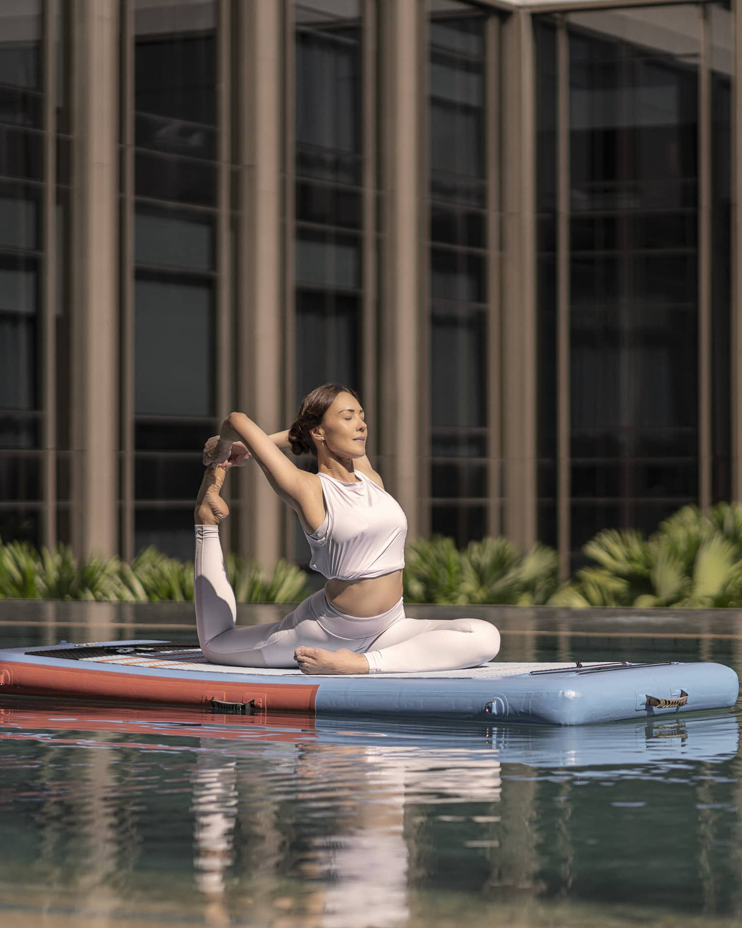 Woman doing a yoga pose on a floating paddle board in hotel pool