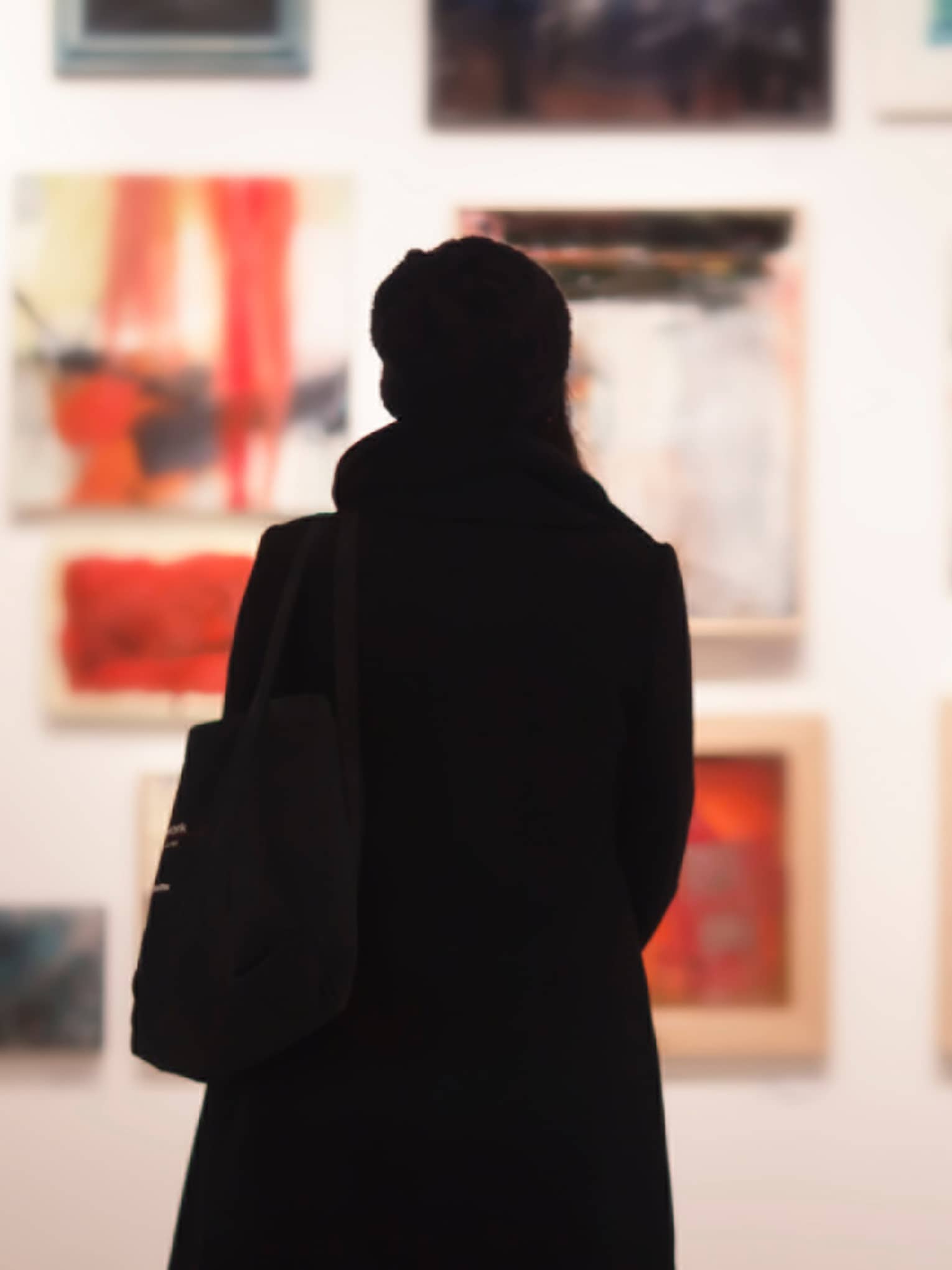 Silhouette of back of woman with hat bag looking at gallery wall with colourful art