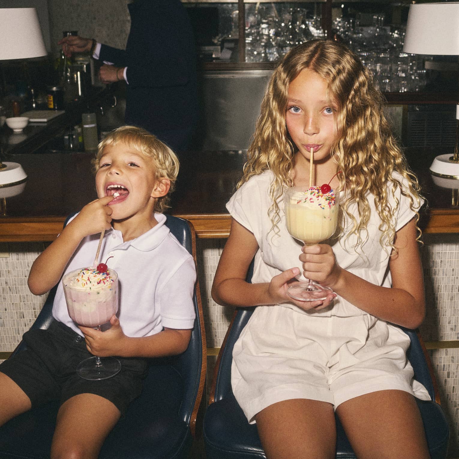 Two children sit on counter stools sipping on large milkshakes