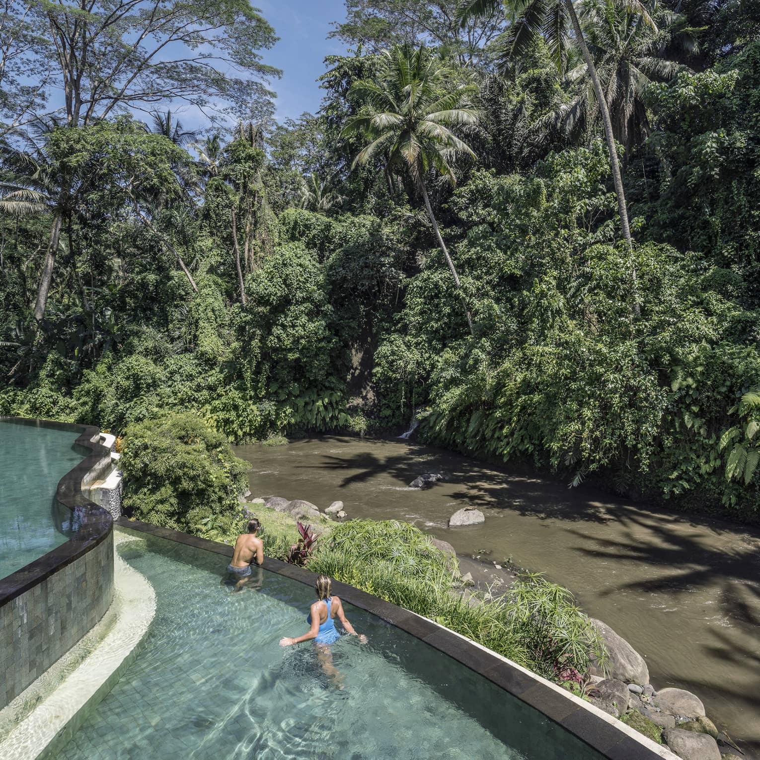 Hotel guests swimming in a pool, overlooking a river in Bali