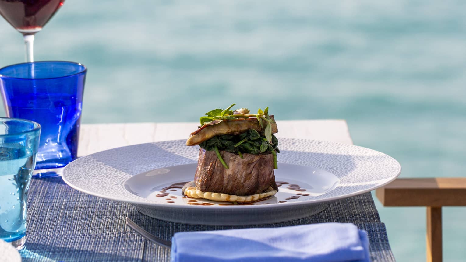 A table with a glass of red wine and a beef dish overlooking the ocean at Four Seasons Maldives - Landa