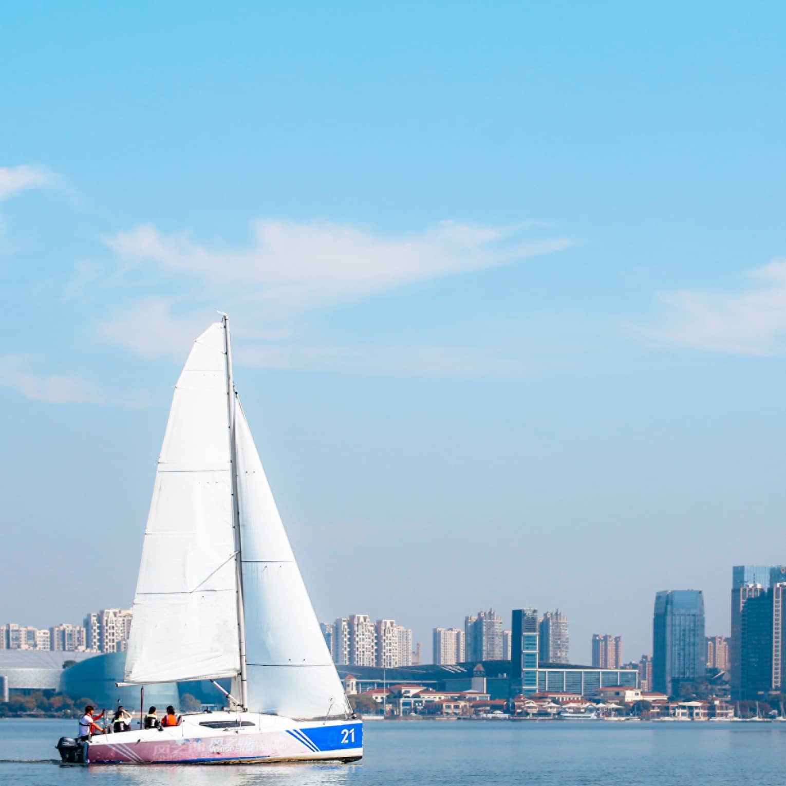 Passengers sailing across the water in a sailboat with the city skyline lining the edge of the water in the background.