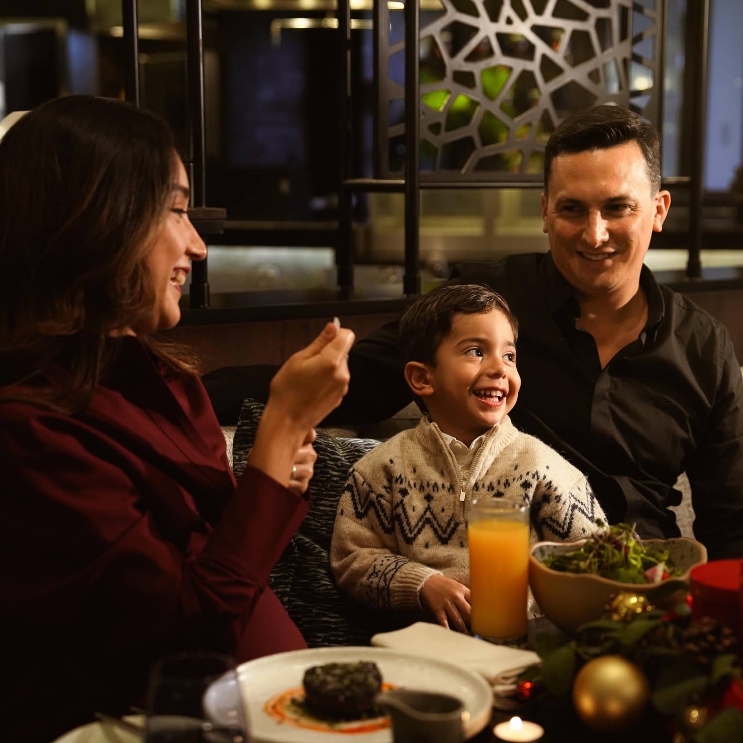 Two adults and a young child sit together in a restaurant booth
