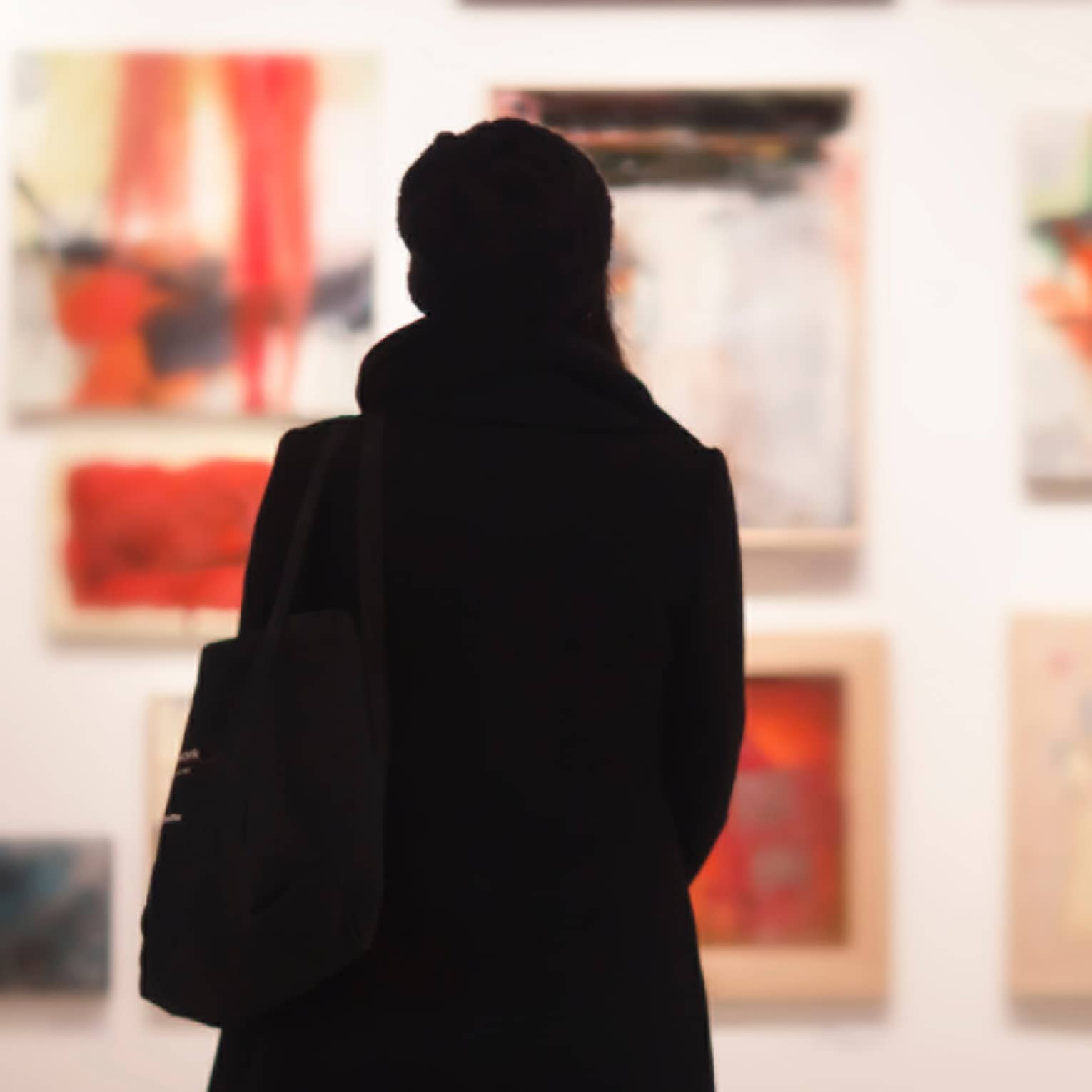 Silhouette of back of woman with hat bag looking at gallery wall with colourful art