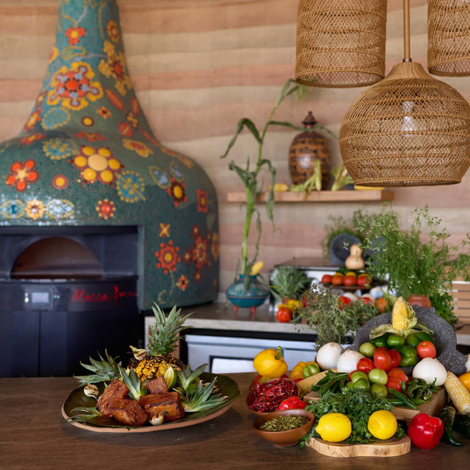 A kitchen with colourful mosaic wood-burning oven, and fresh fruit and vegetables on the table