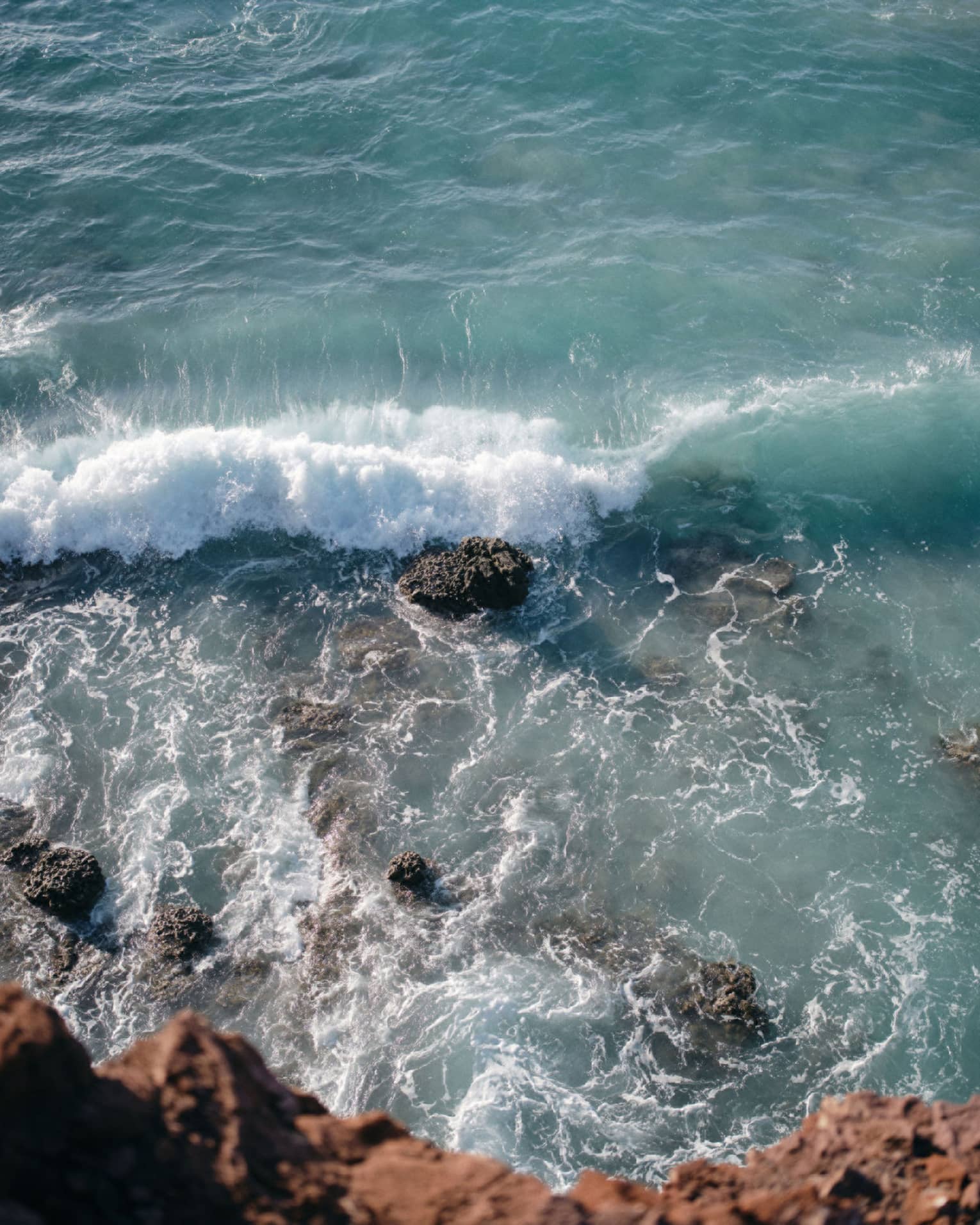 Aerial view of an ocean wave breaking over a rock formation
