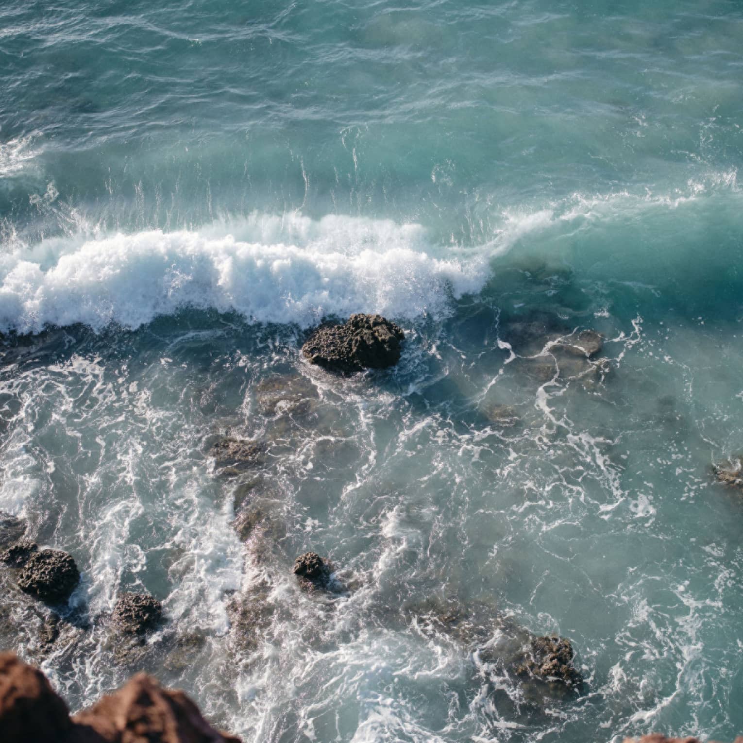 Aerial view of an ocean wave breaking over a rock formation