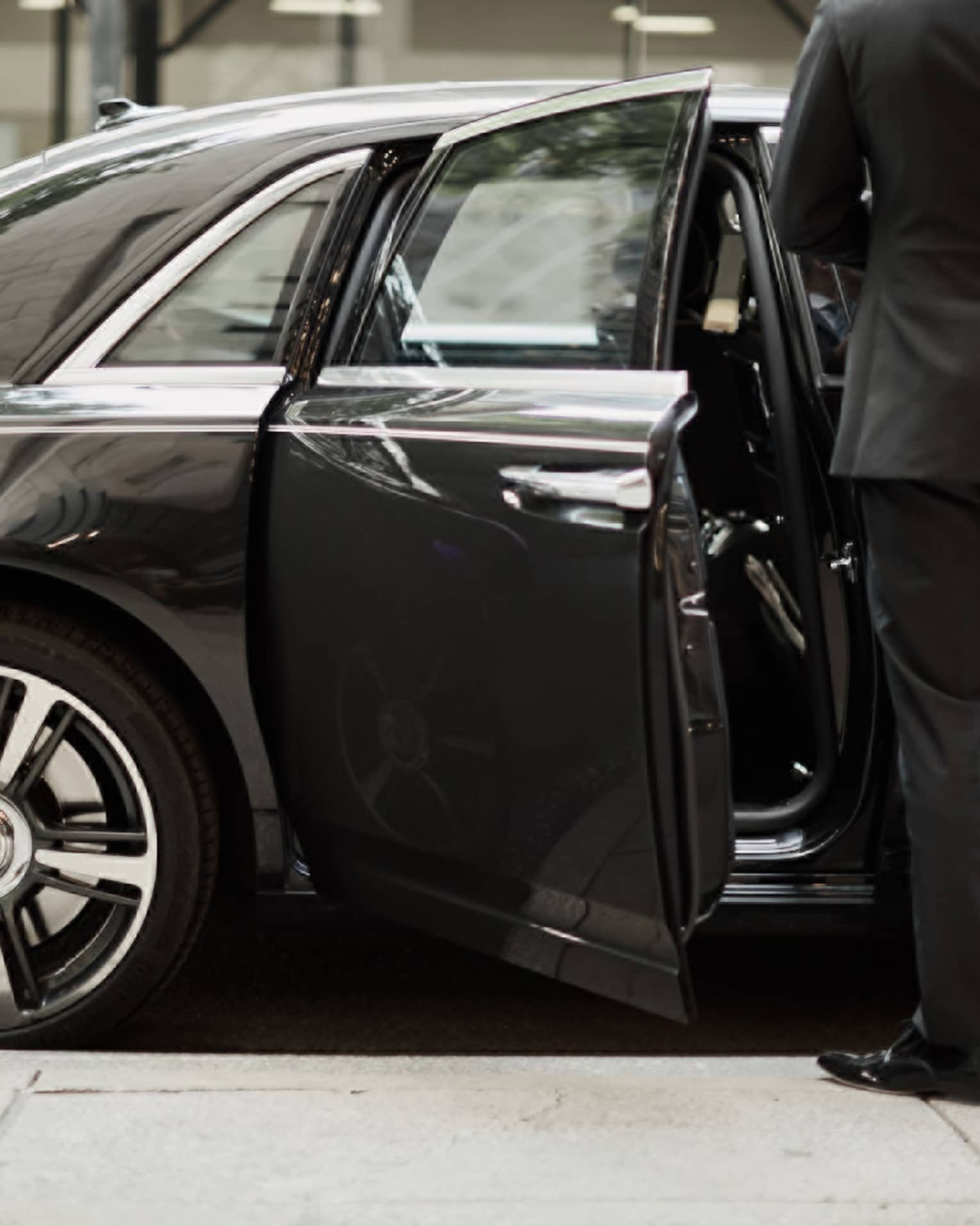 Man in suit by open door of black luxury car