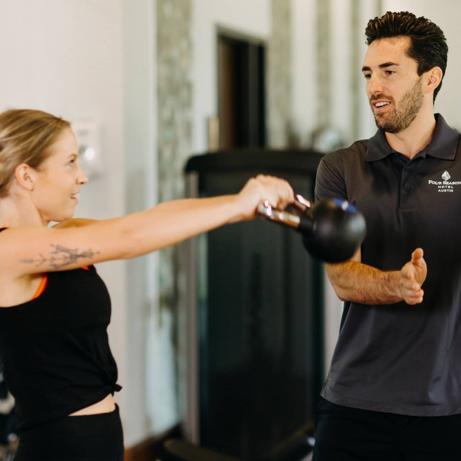 Male fitness trainer works with female guest who is using a kettlebell