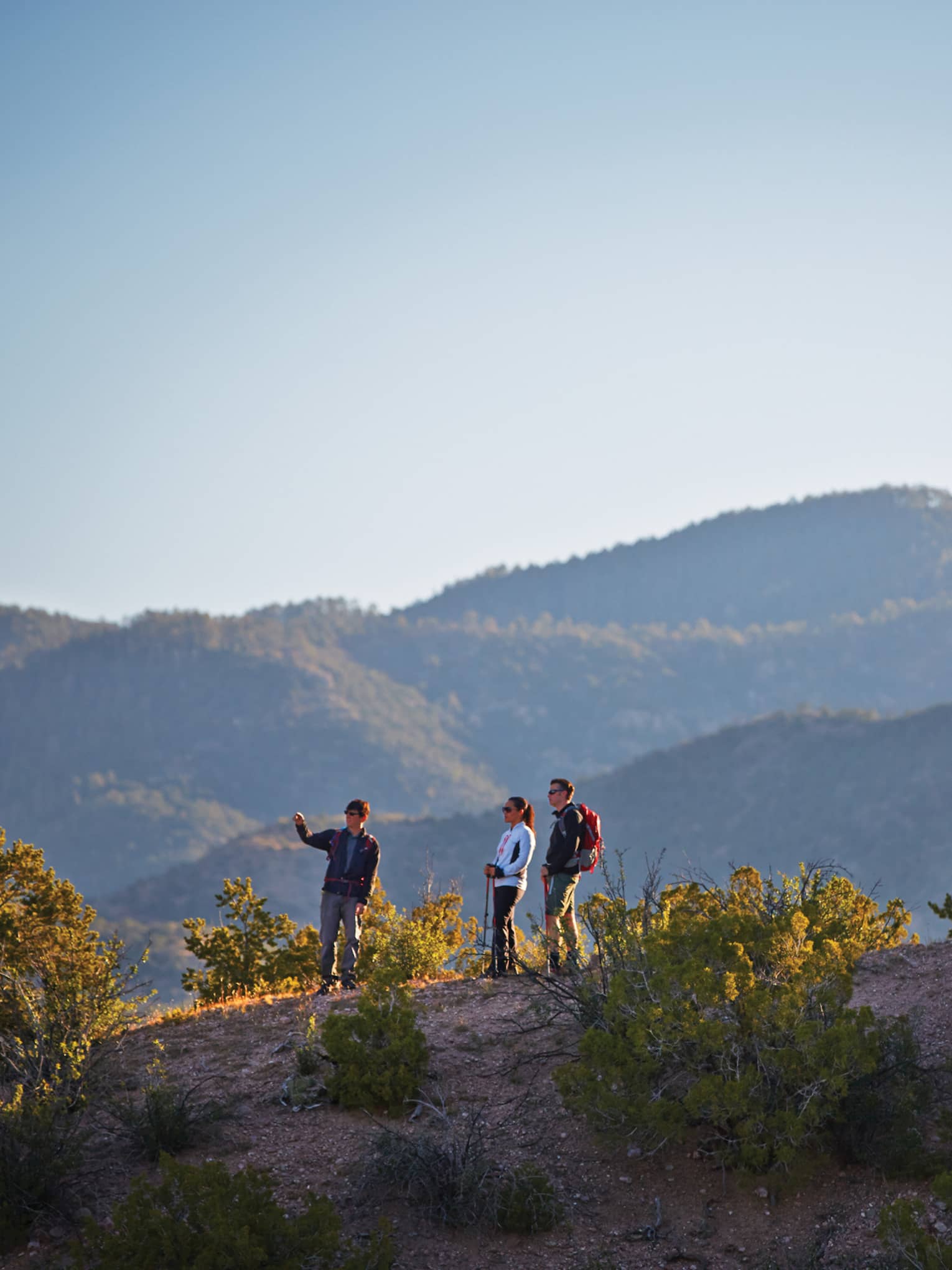 Three people hike on desert mountain hill