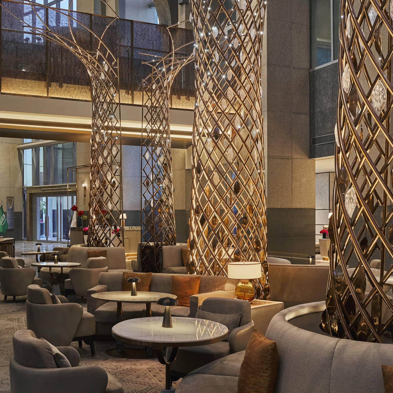 Hotel lounge with towering ceilings, large connical metal tree sculptures surrounded by plush seating and various tables and chairs