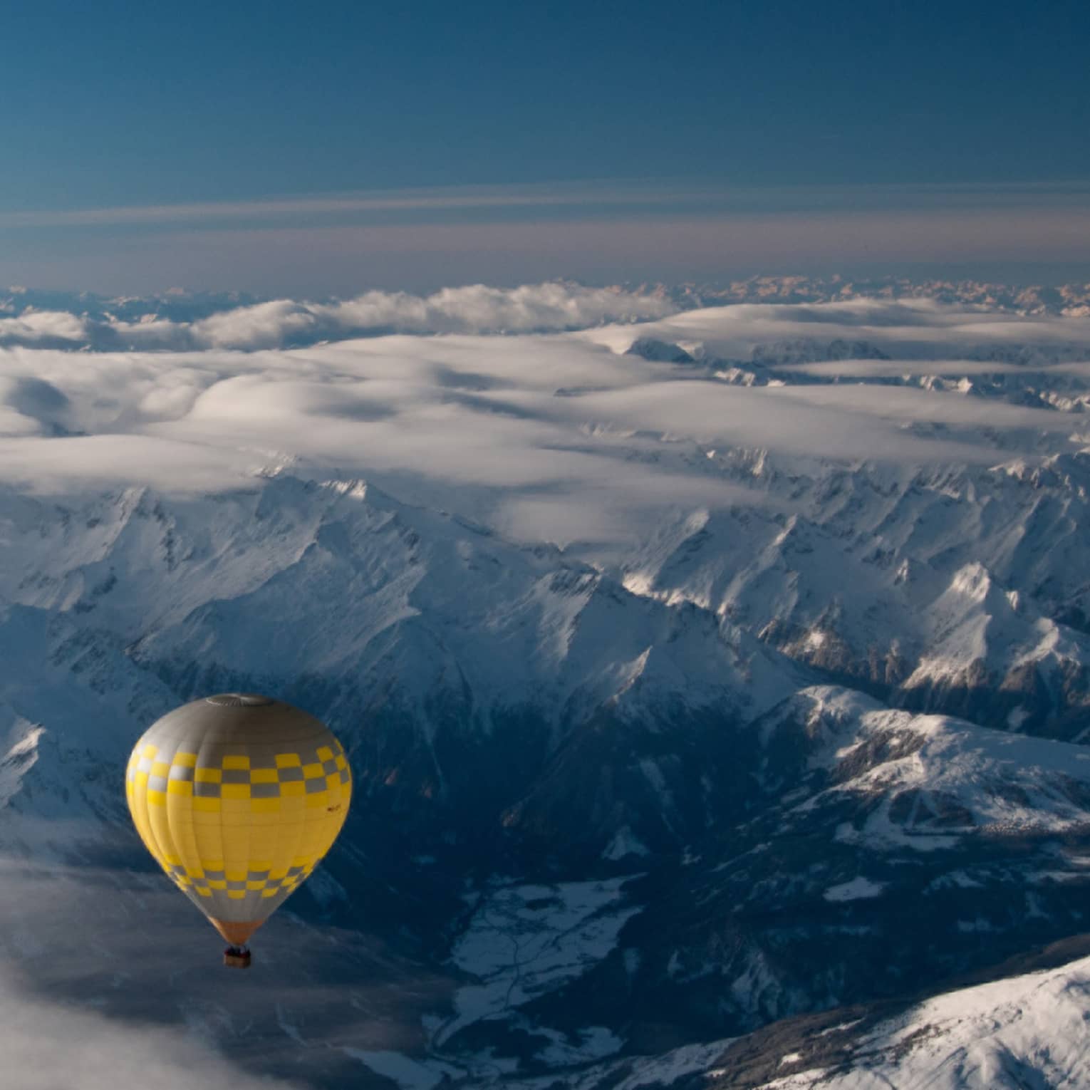 Yellow hot air balloon soaring over the snow-covered Alps