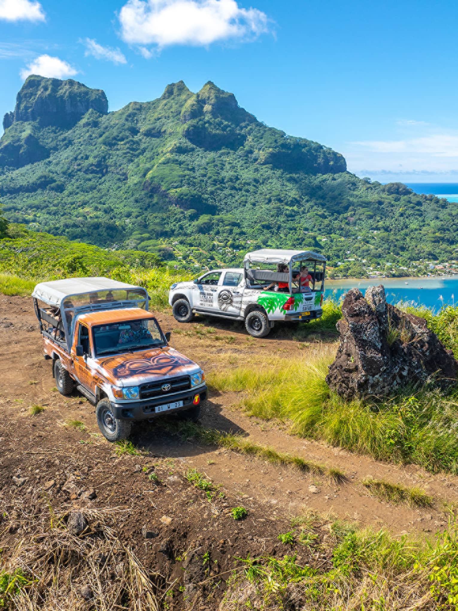 Two trucks parked on dirt path with green mountain looming in background