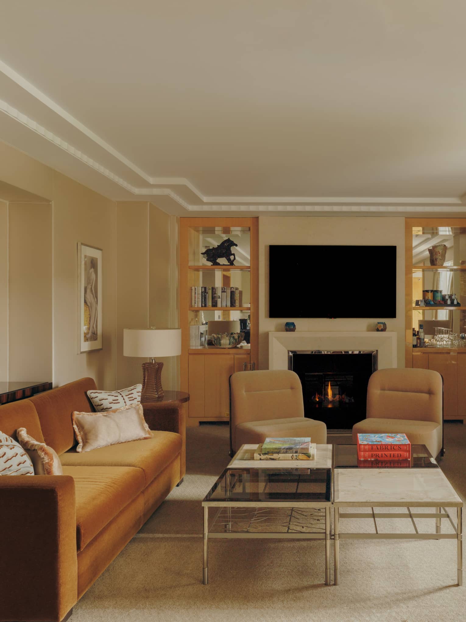 Luxury hotel suite living room, with two tan sofas facing each other, plus two arm chairs, TV and fireplace