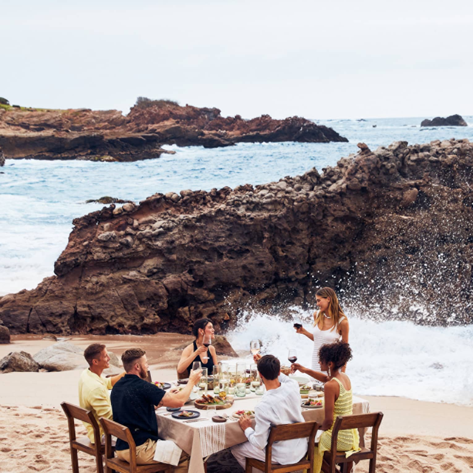 A group eating at a table on a beach with waves crashing nearby.