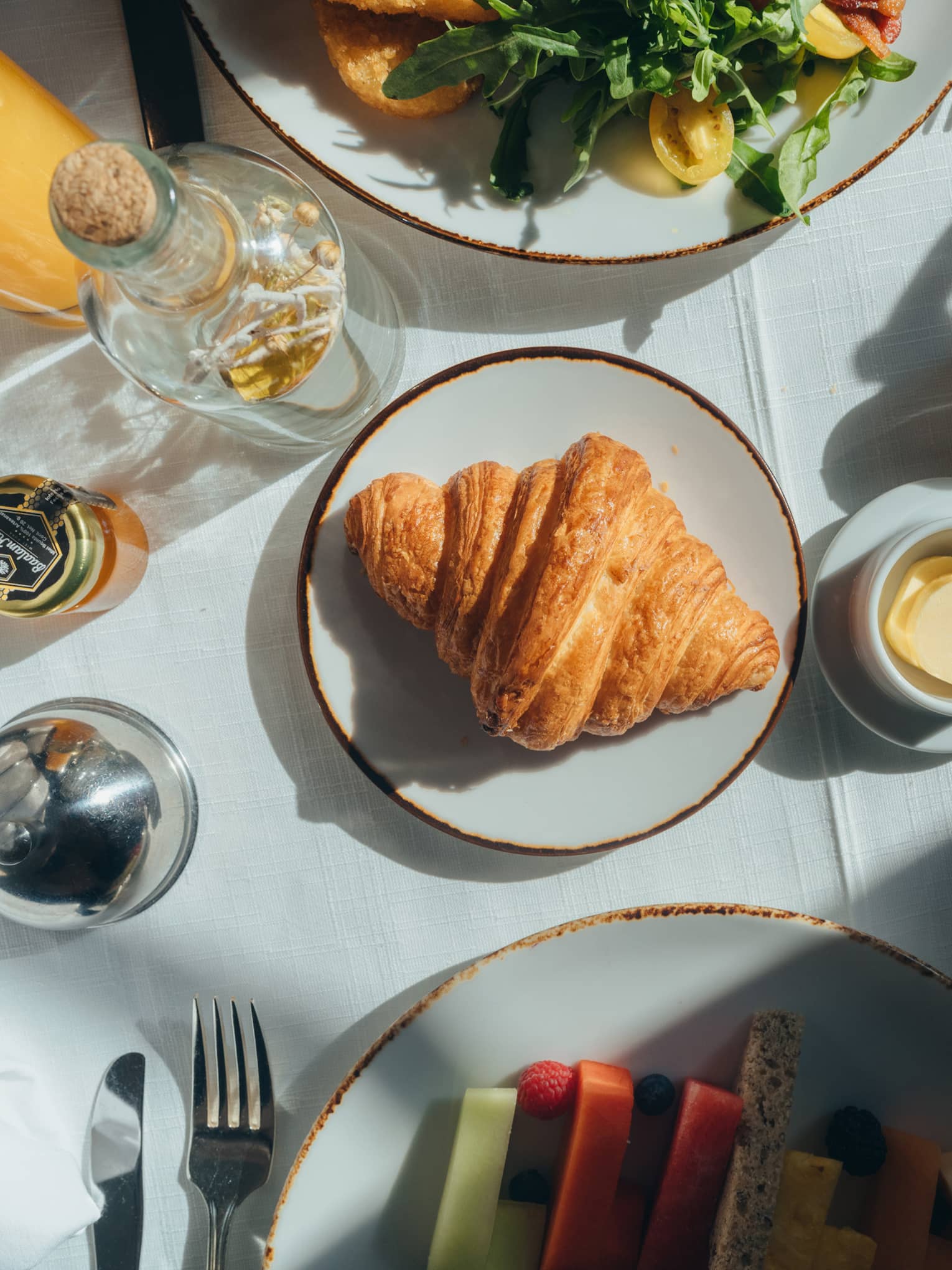 View from above of various plated food items, beverages and utensils on a table with a white tablecloth