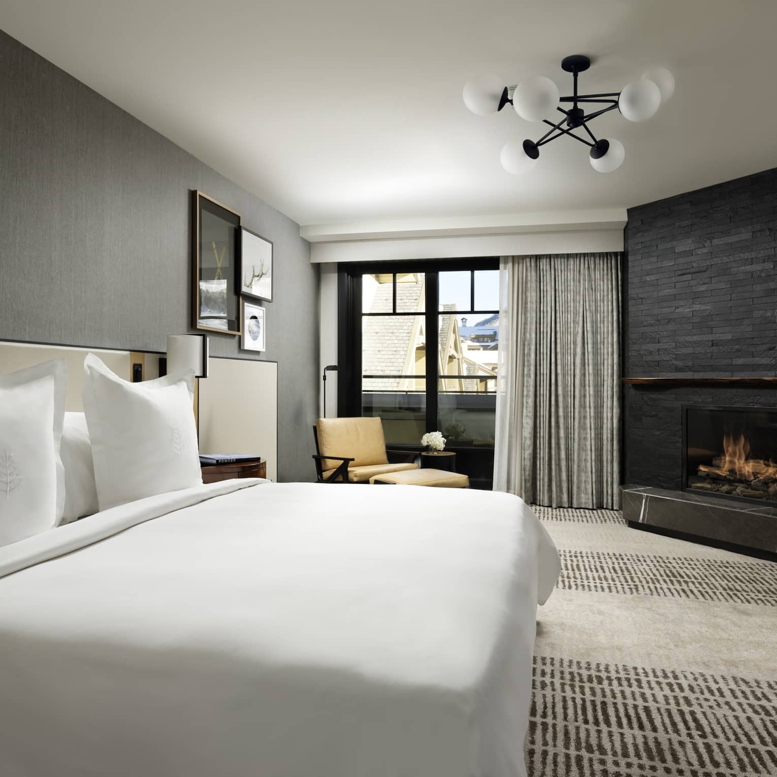 One-bedroom suite with King bed, corner fireplace, floor-to-ceiling window with grey curtains, yellow chaise