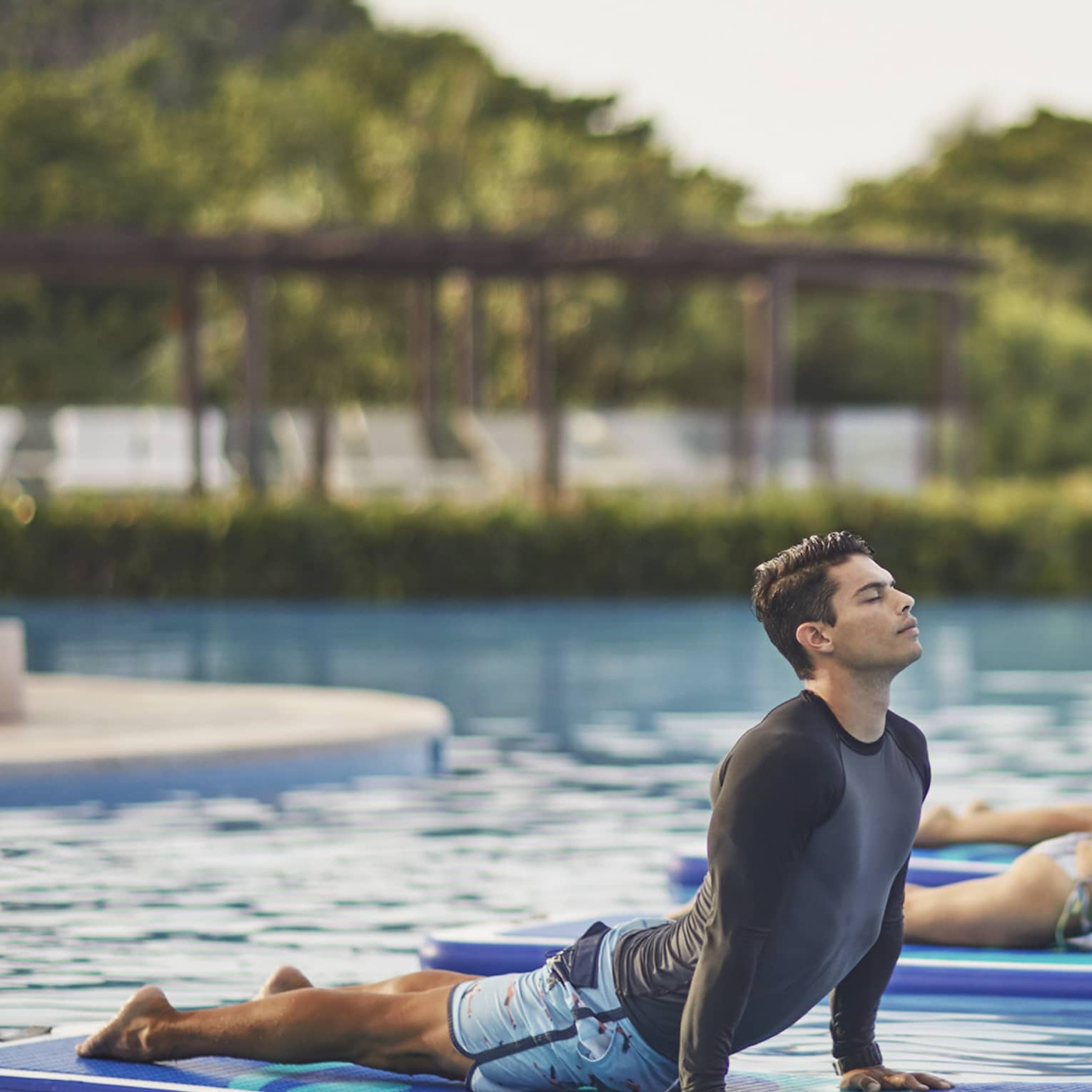 Man, two women in yoga poses on paddle boards on swimming pool