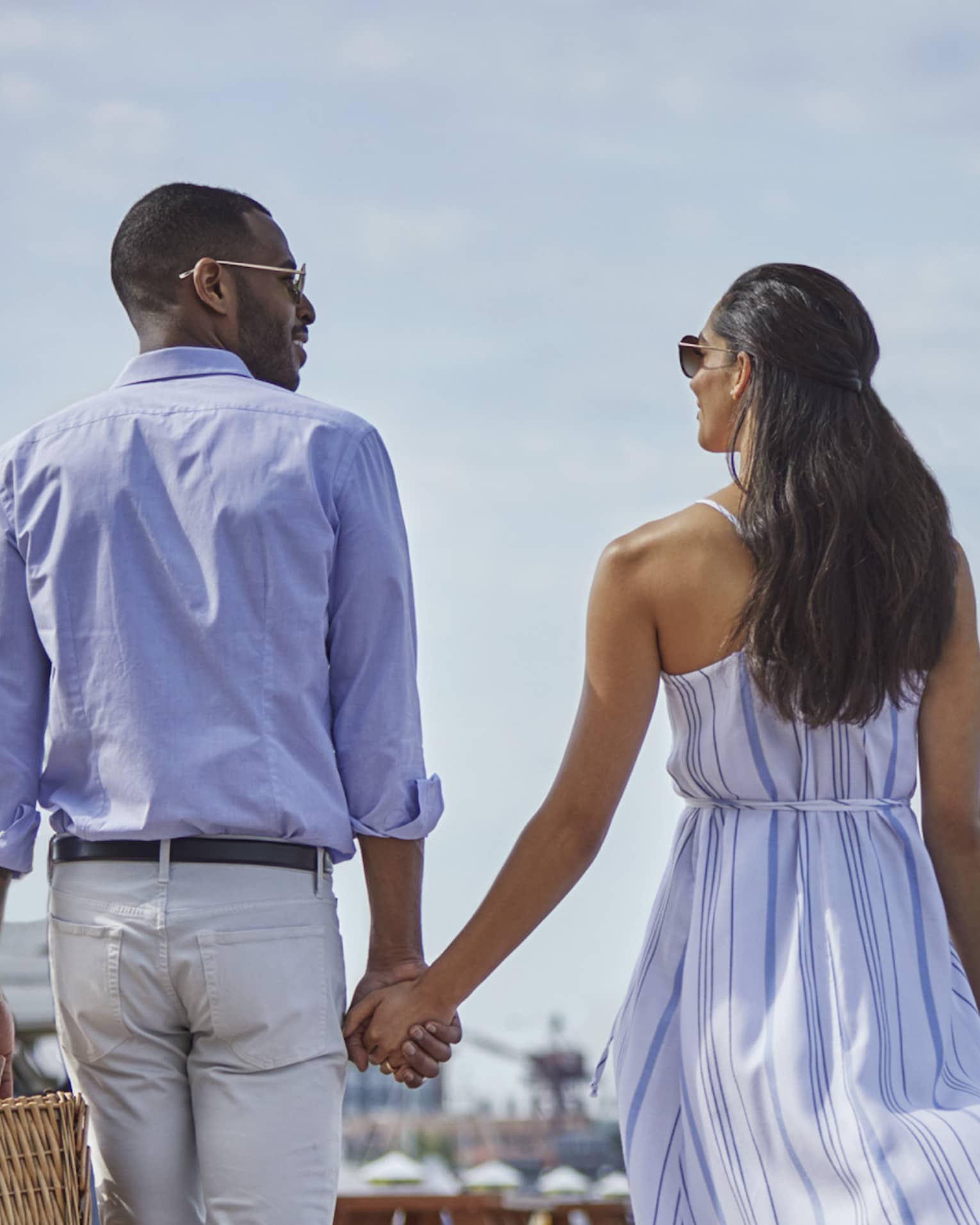 Back of man and woman holding hands, walking along dock near sailboat