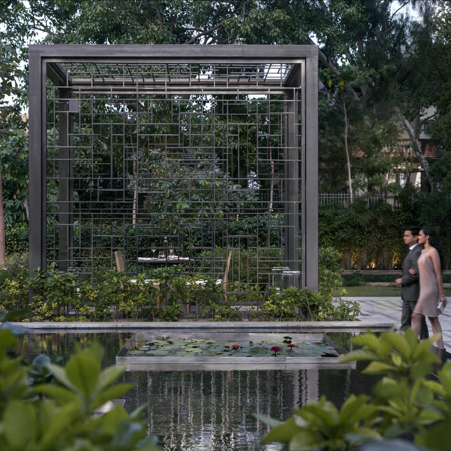 A couple walks through a dining area in a garden with lily pads and a waterfall
