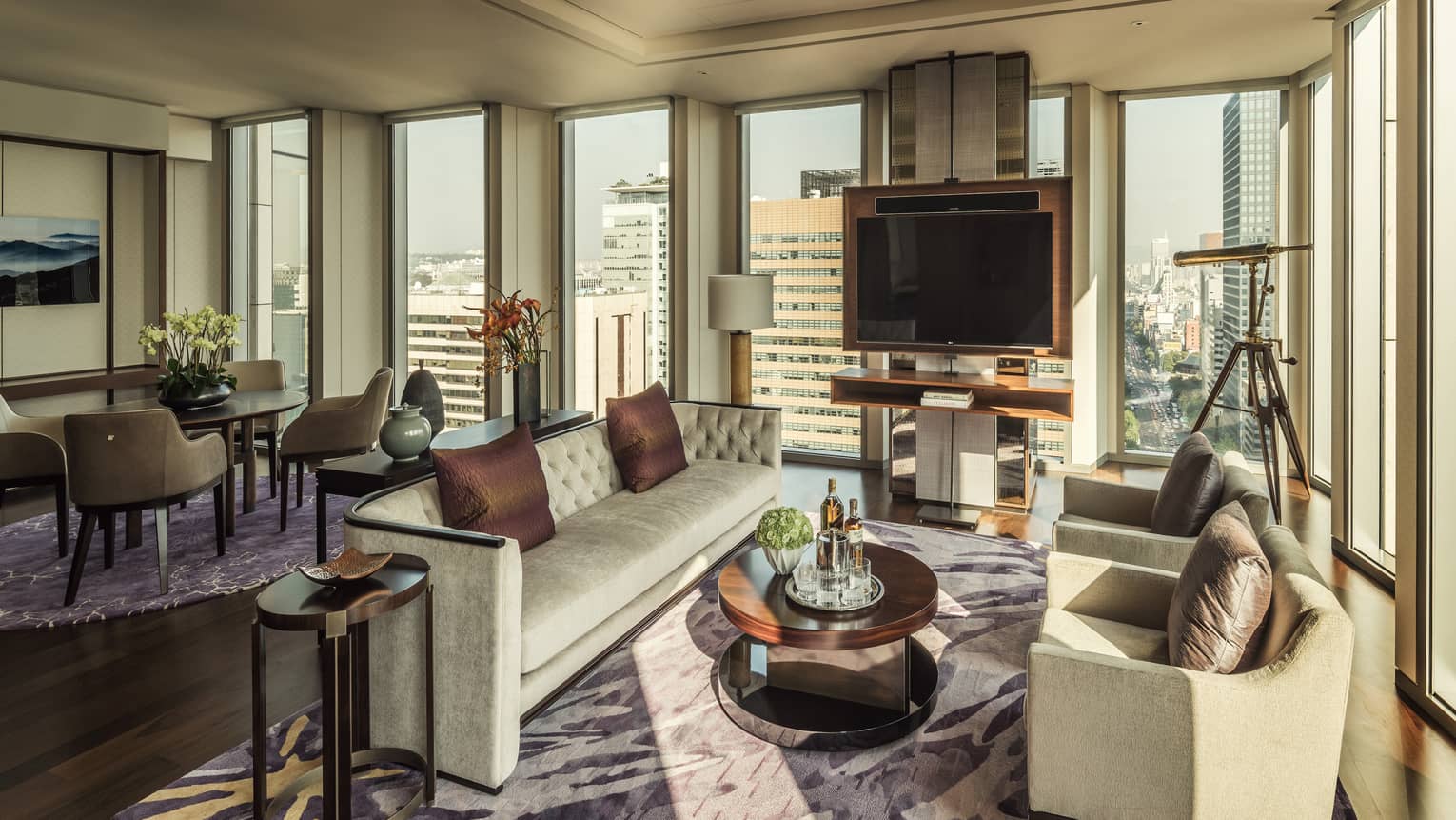 Ambassador One-Bedroom Suite long sofa, brown silk pillows, two armchairs around table with liquor, corner windows and telescope