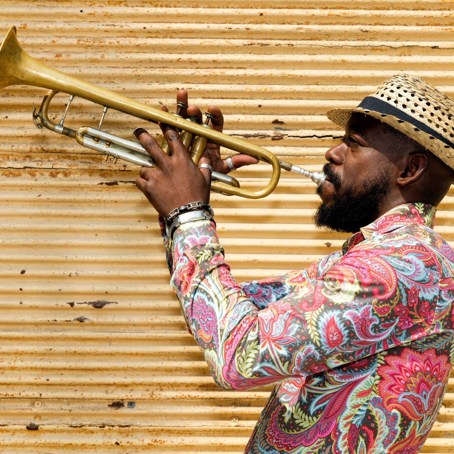 A man in a hat and colourful shirt playing a trumpet.