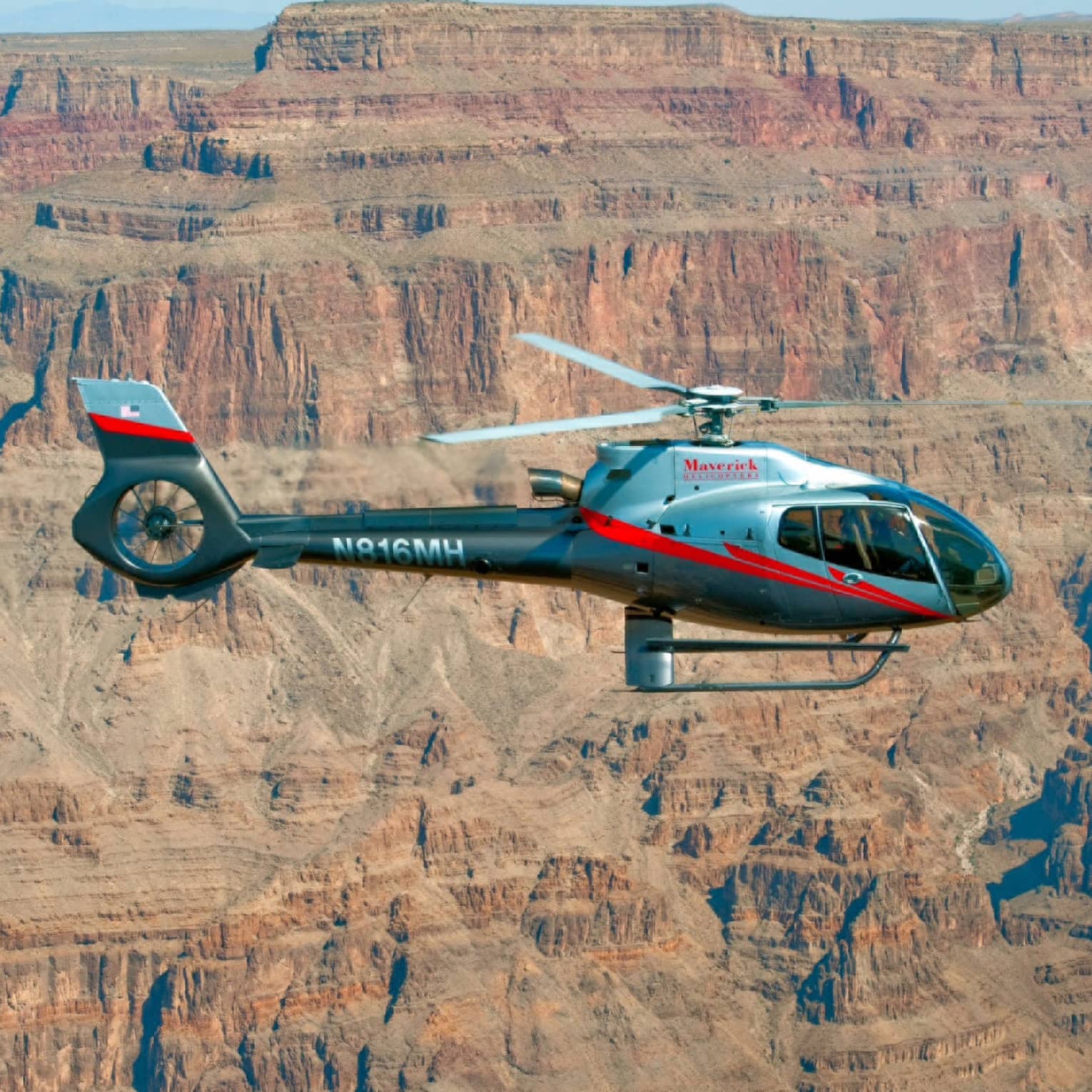 Maverick Helicopter Tours helicopter flying in sky in front of canyon cliffs