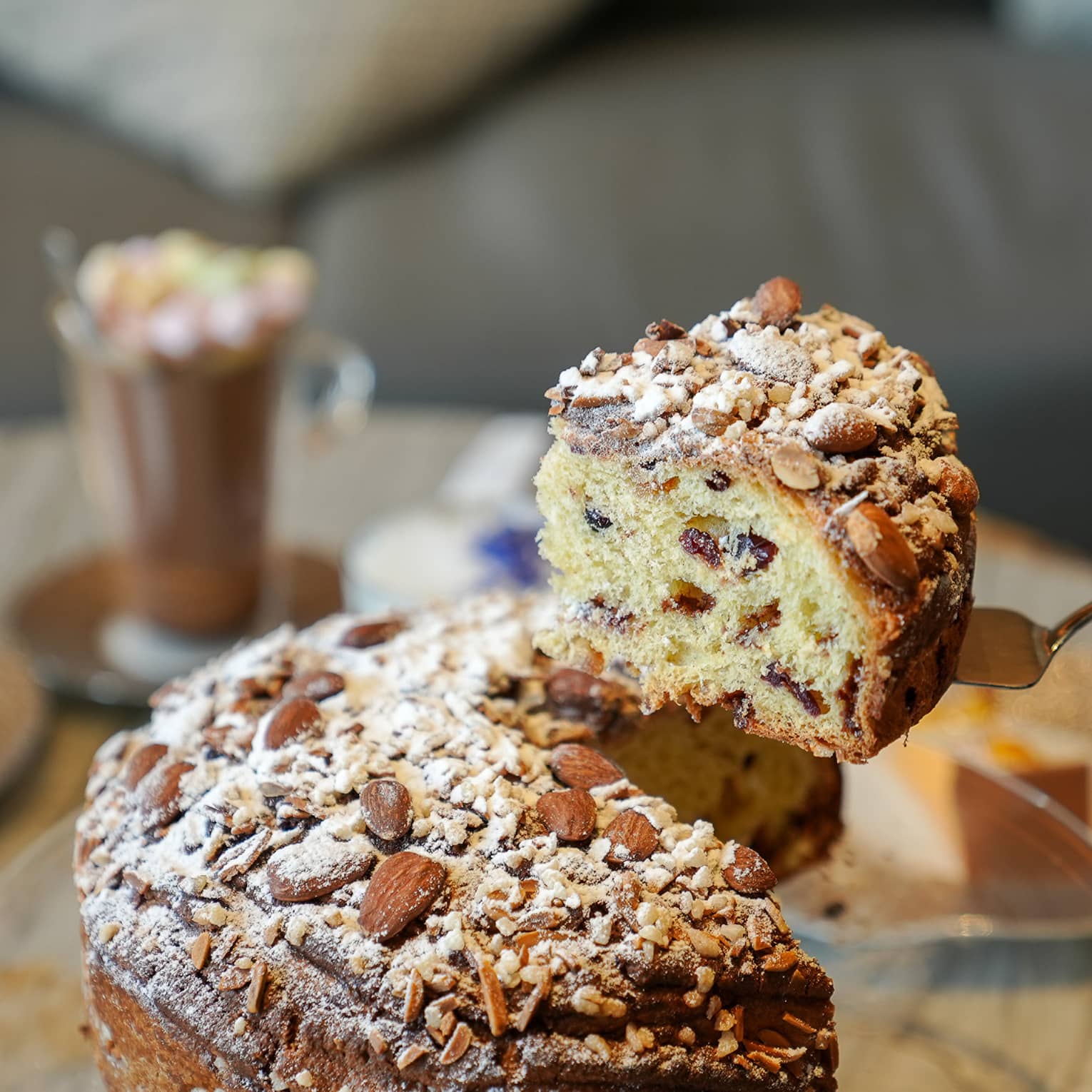 Hand holds up thick slice of powdered sugar?dusted panettone on gold cake server