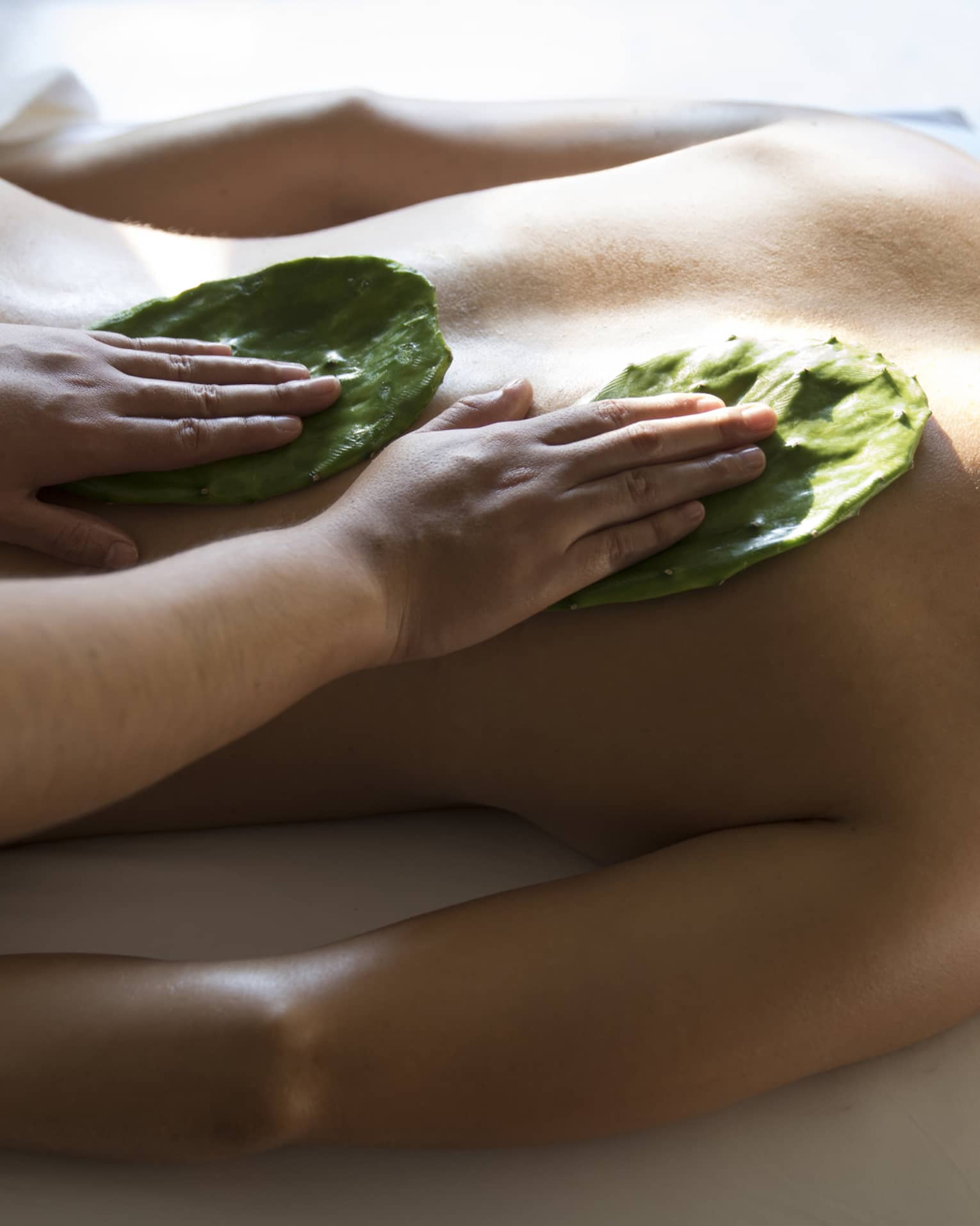 Woman face-down on table as masseuse rubs Nopal cactus leaves on her back with Mexican Nakieri Treatment