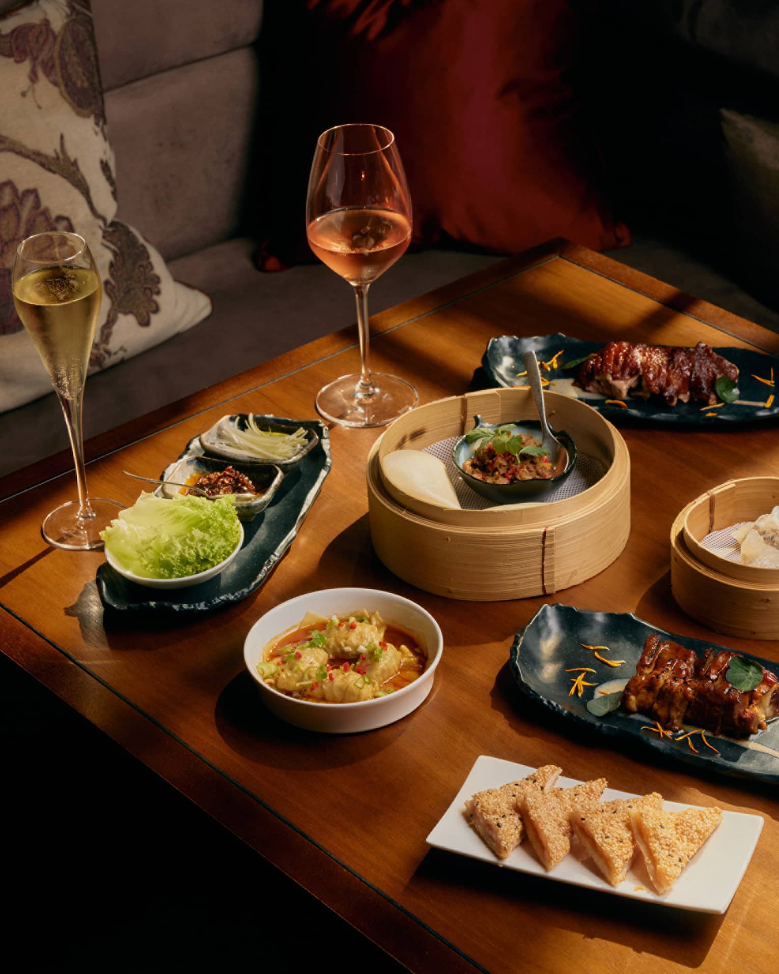 Assorted dim sum and glasses of wine on square wooden table