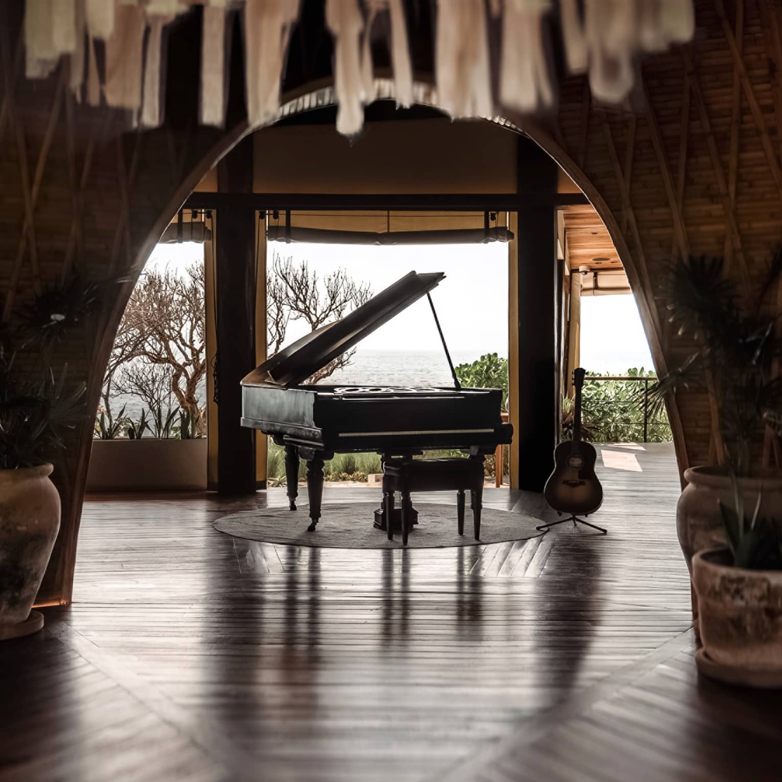 Black grand piano sits in the centre of a room that opens up to the ocean in the distance