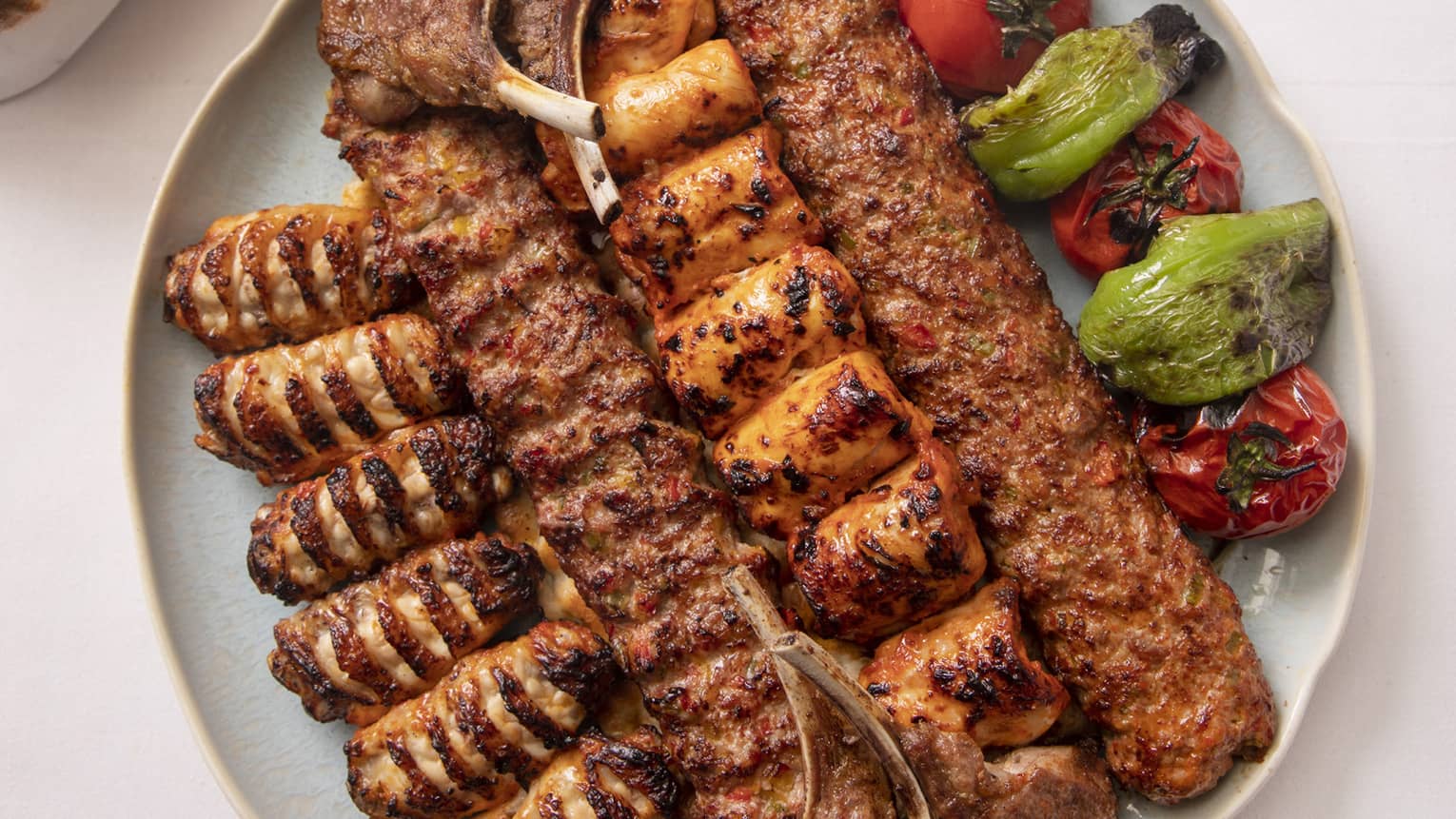 Grilled meat skewers and vegetables on round plate beside flatbread