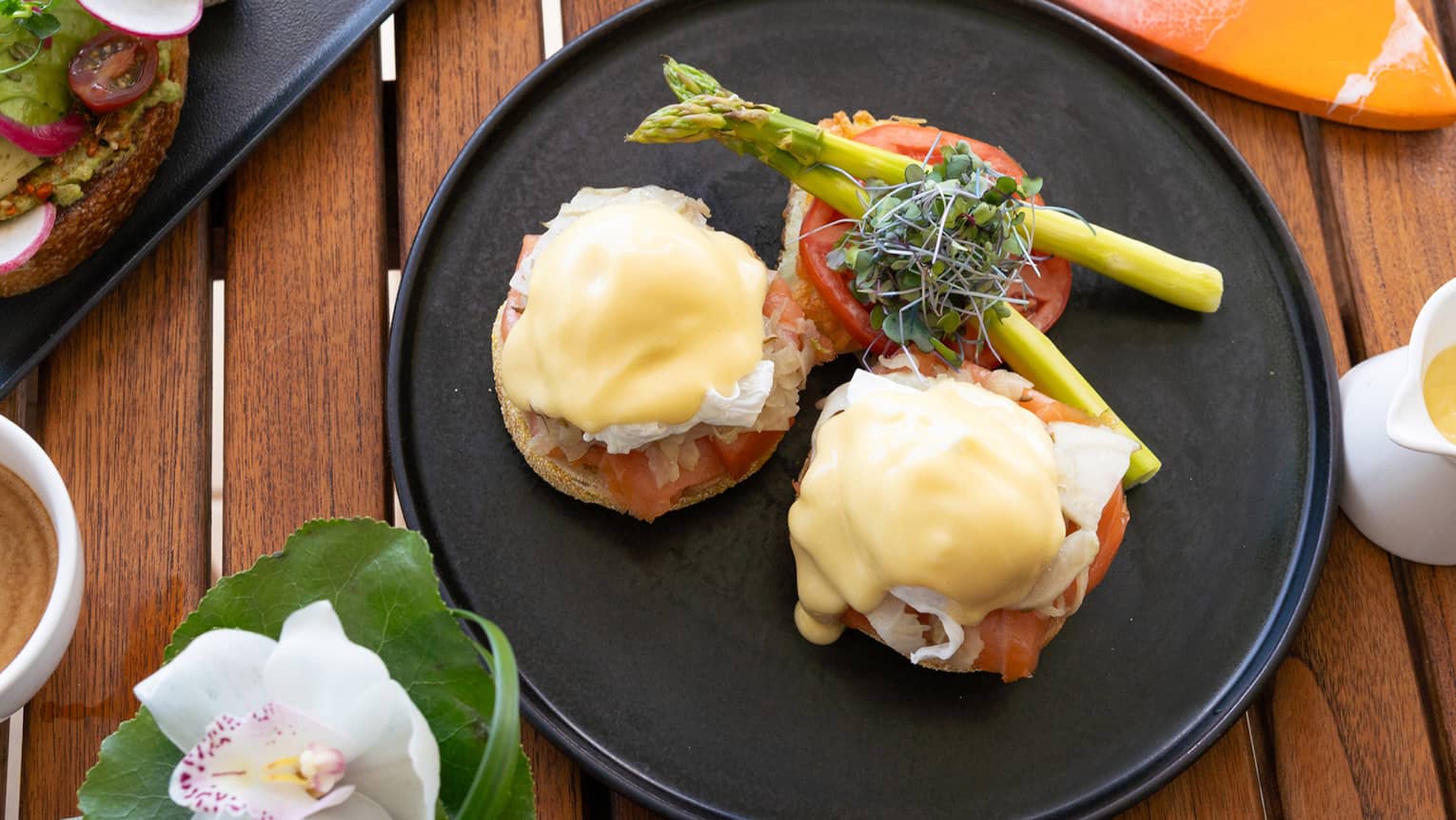 Eggs Benedict, coffee, juice and smoothie with Hawaiian flower on wooden table