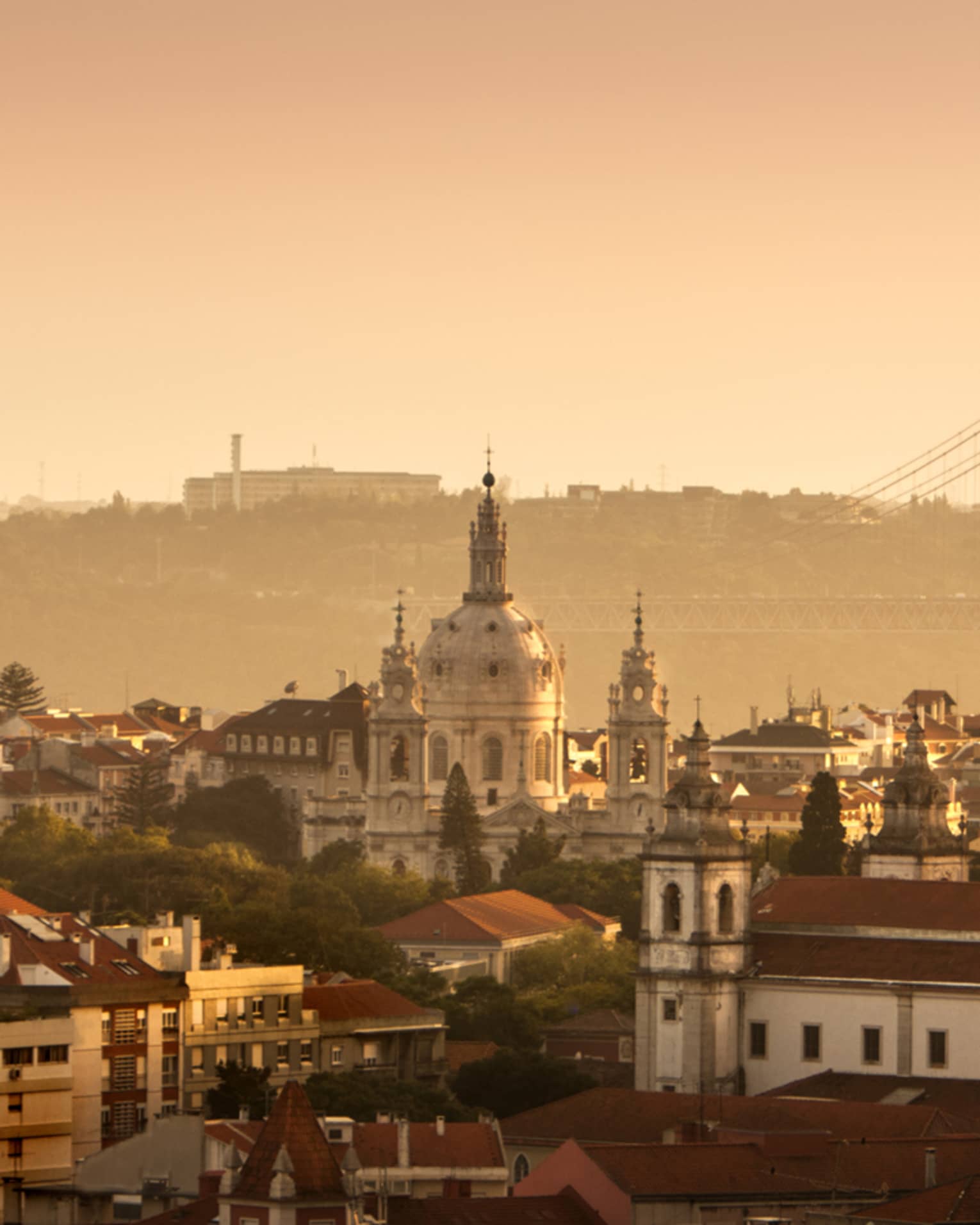 Orange haze over Lisbon buildings, skyline and bridge at sunset