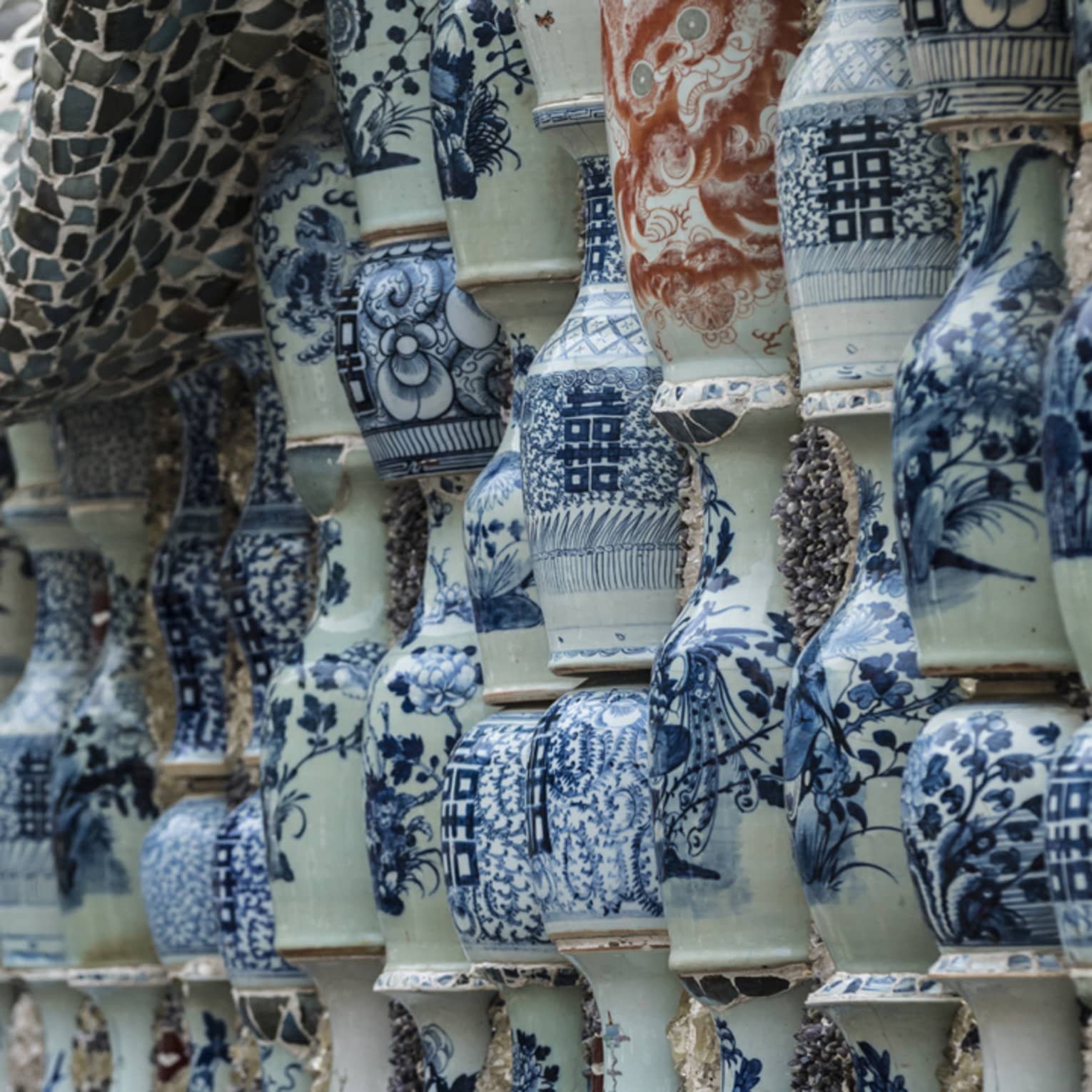Stacks of porcelain vases with blue hand-painted designs are embedded in a wall topped with a wavy stone mosaic overhang. 