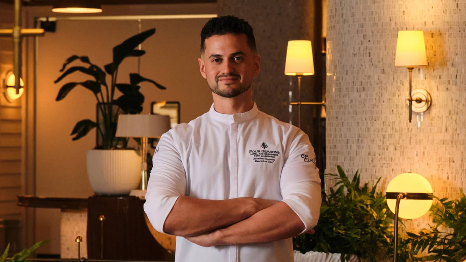 A chef stands in an elegant, softly lit indoor dining space.