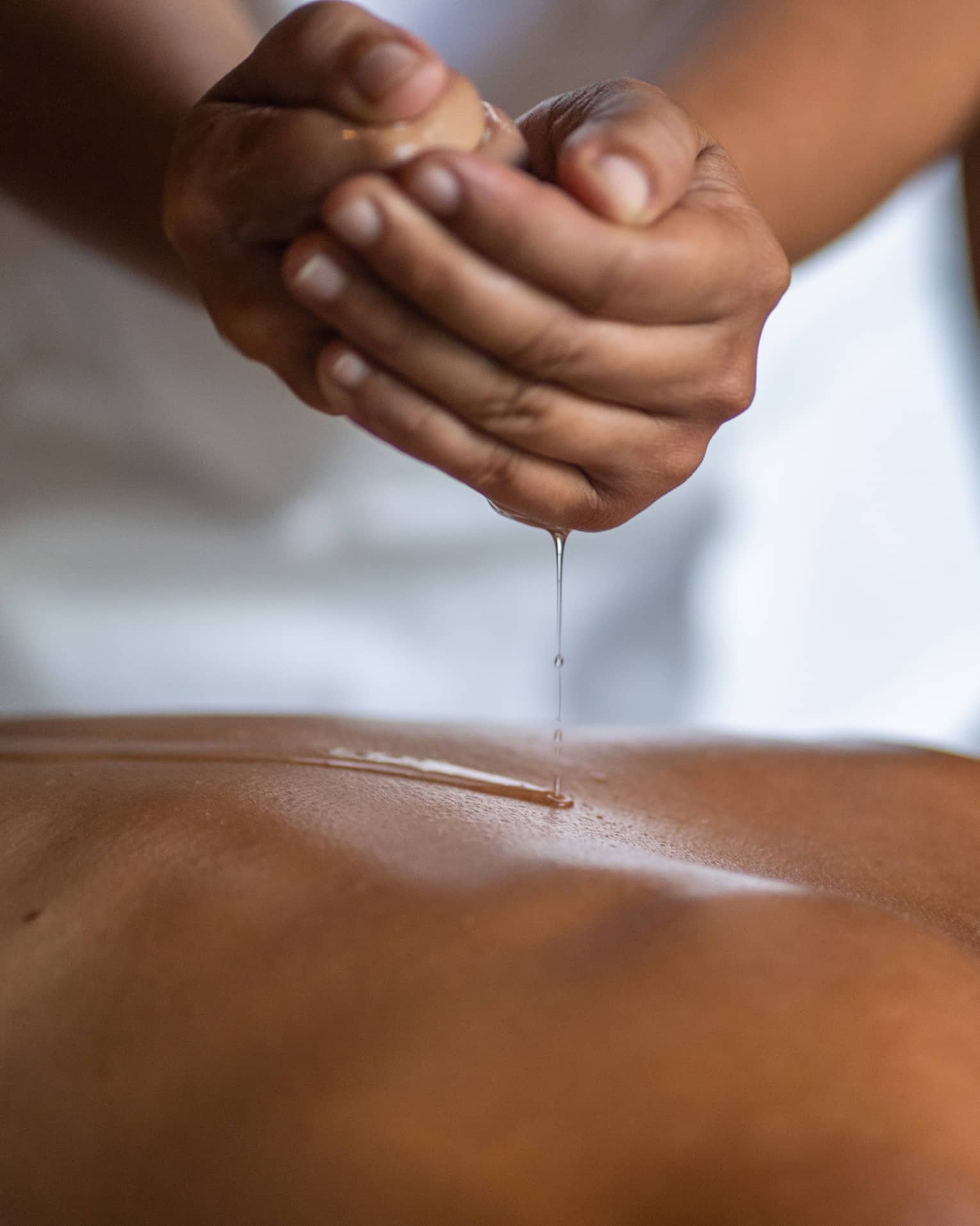 Delicate hands apply oil to a guest's back during a spa treatment