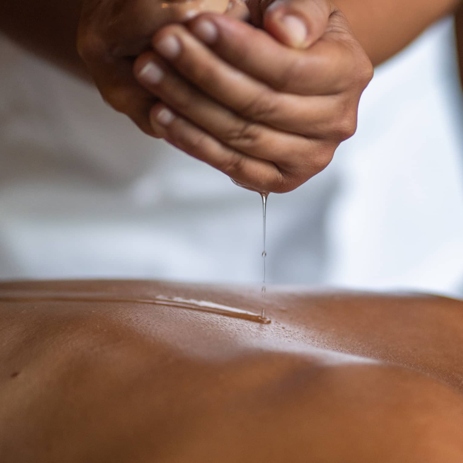 Delicate hands apply oil to a guest's back during a spa treatment