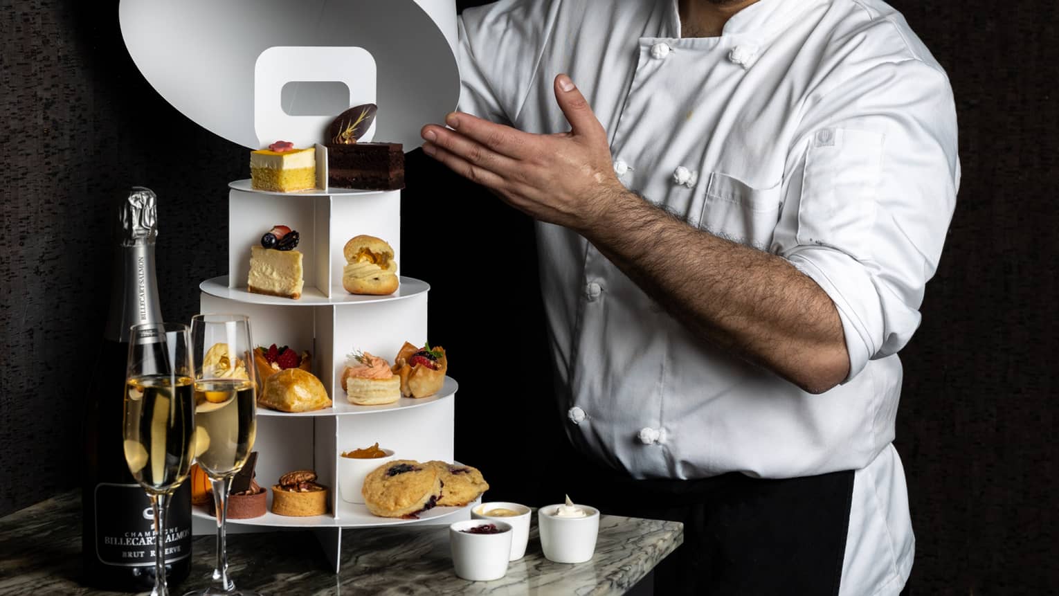 A chef revealing a three-tiered display of pastries and sweets.