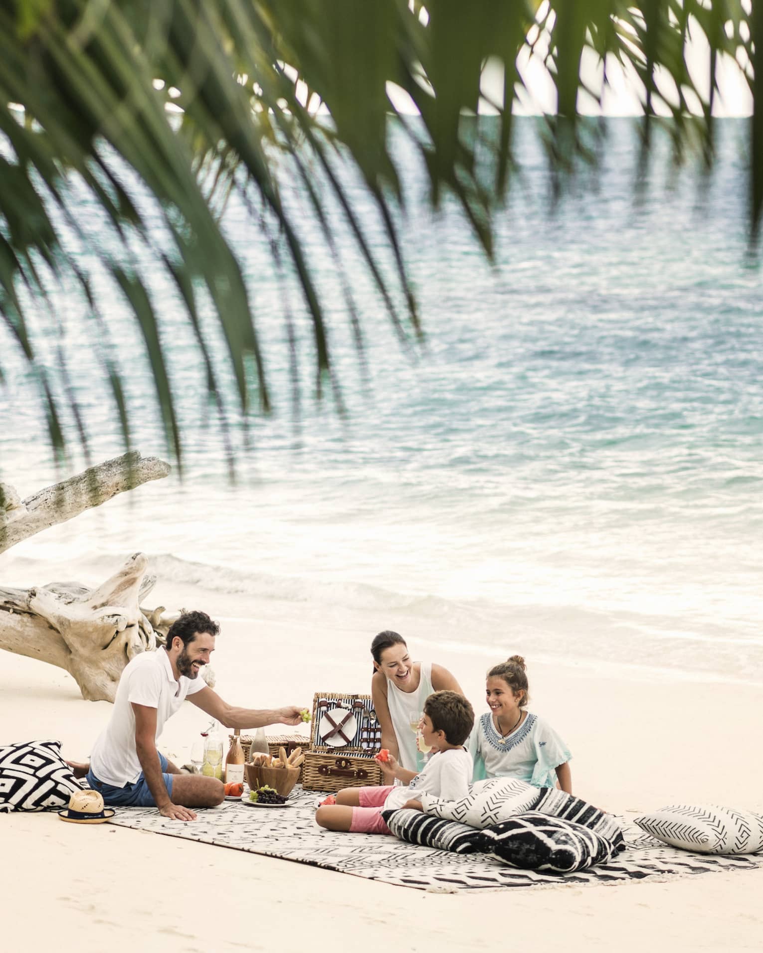 A man, woman and two children picnic on the beach just a couple feet away from the ocean. 