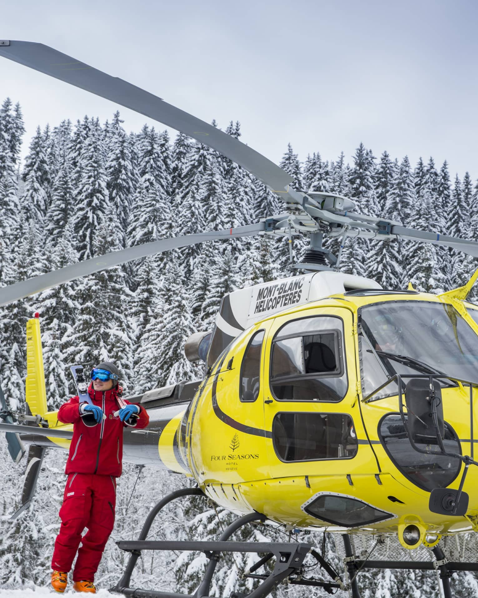 A yellow helicopter rests atop a snow covered mountain in Megeve