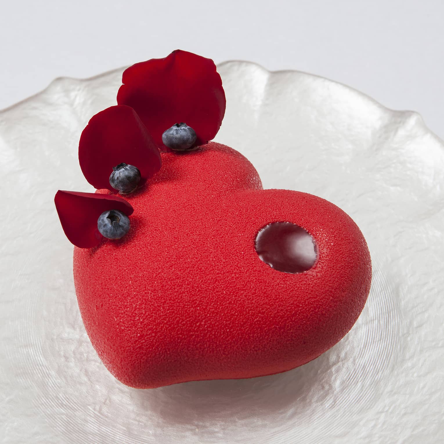 Valentine's Day heart-shaped cake on pearlescent plate with rose petals and blueberry garnishes