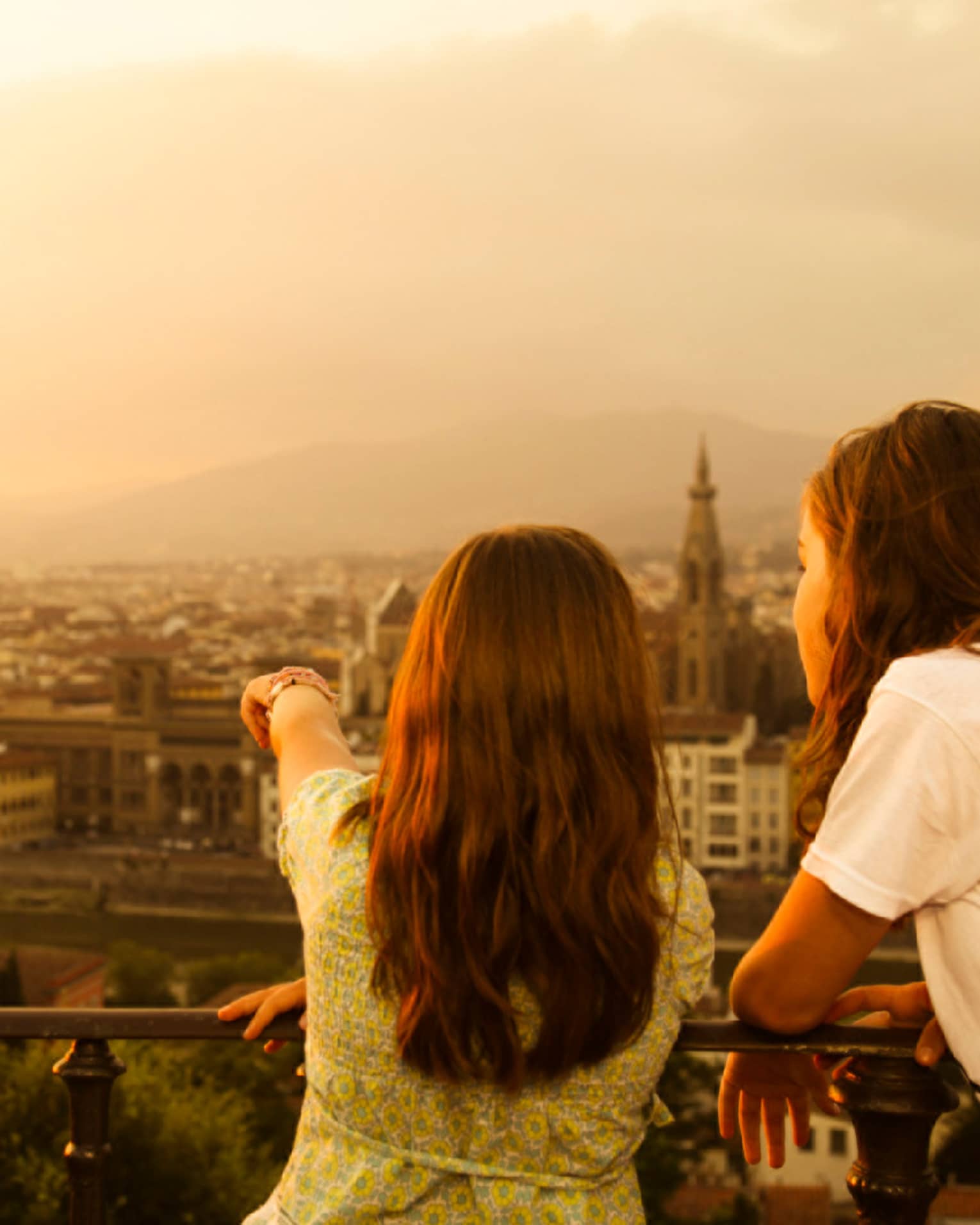 Back of two young girls looking out over Florence skyline, rooftops, Duomo at sunset